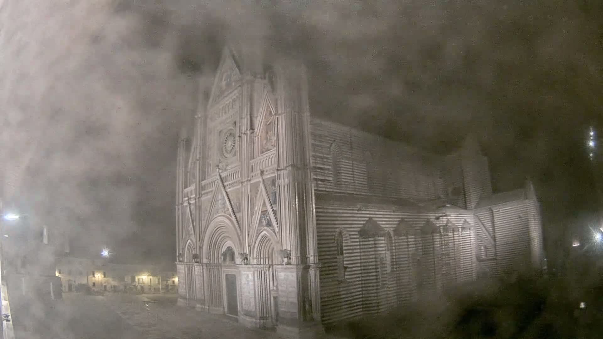 A large, ornate striped stone building, possibly a cathedral, is partially obscured by heavy fog or mist at night.