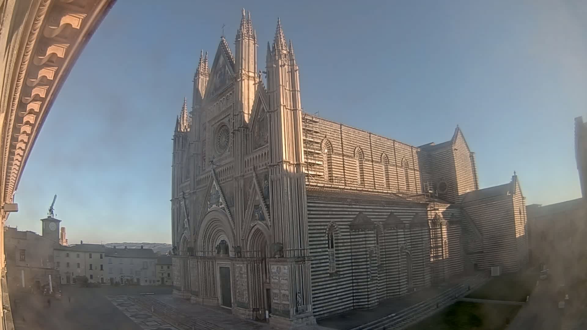 A large, striped cathedral stands in a town square under a clear, bright sky.