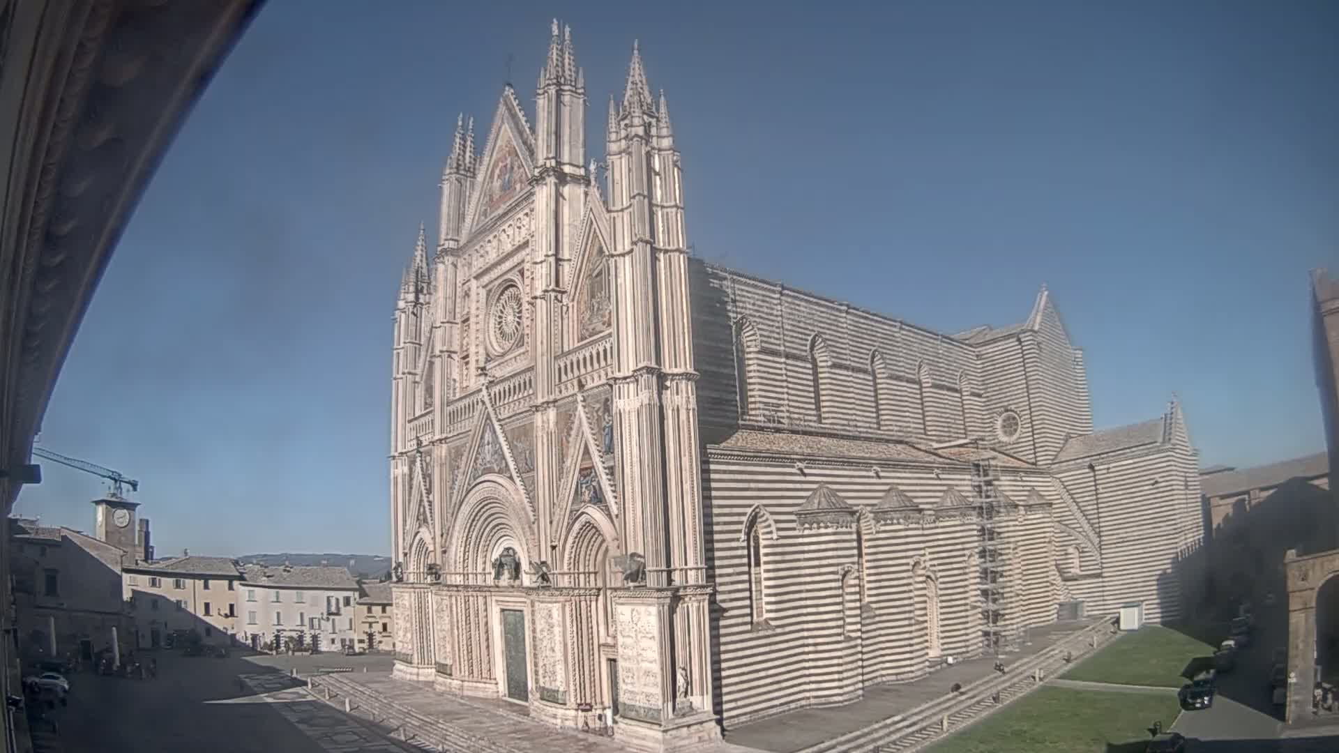 A large, striped cathedral with Gothic detailing stands in a town square on a clear, sunny day.