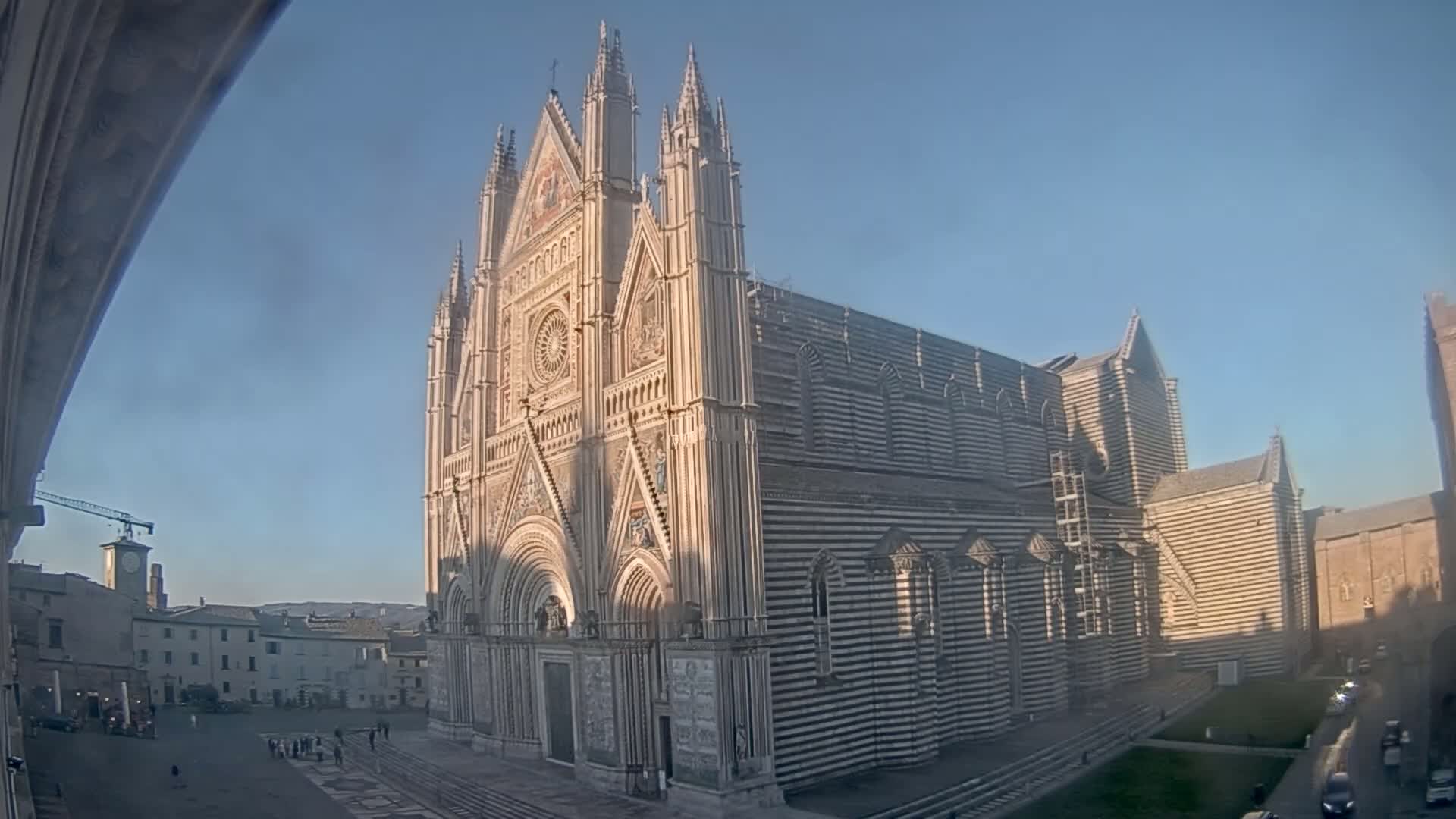 A large, ornate cathedral with black and white striped exterior walls stands in a city square on a clear, sunny day.