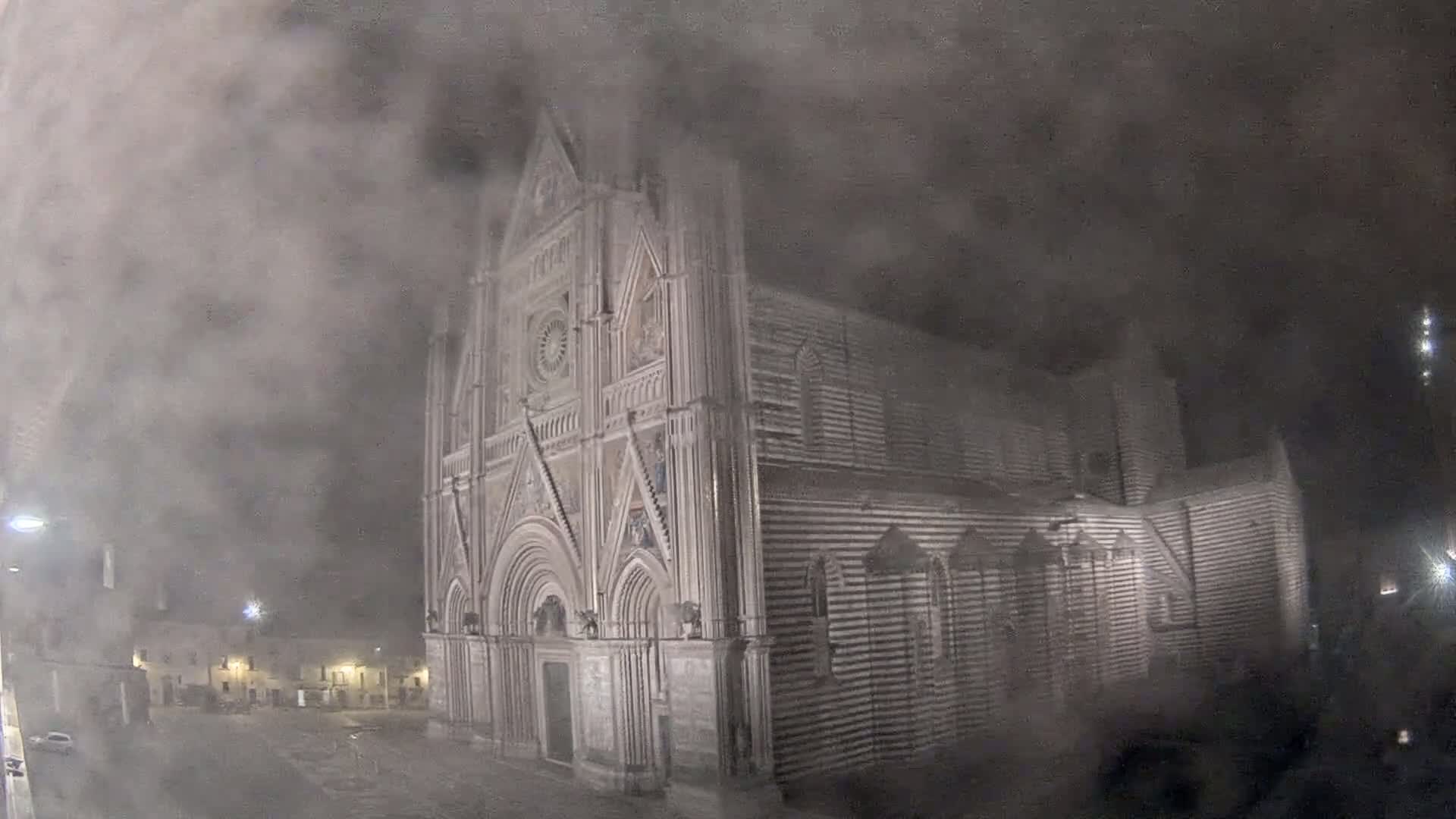 A large, ornate cathedral stands at night in a thick fog.