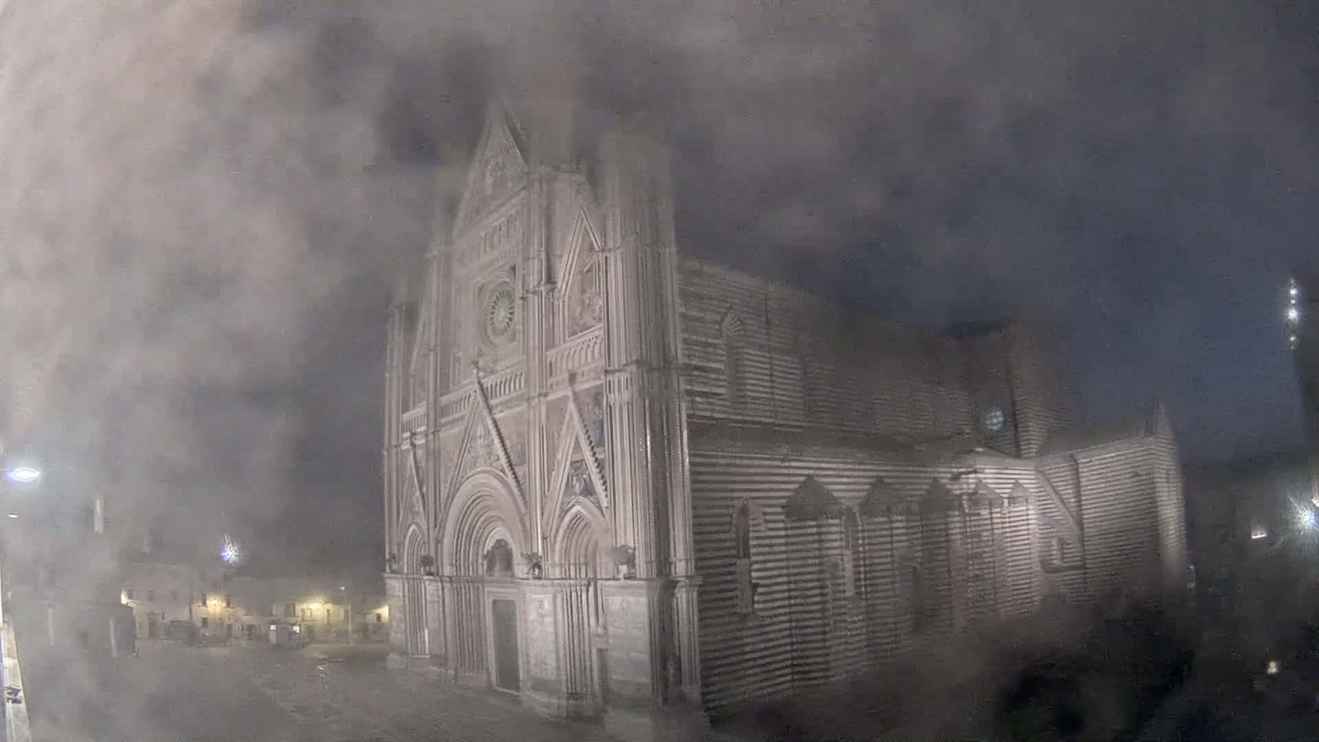A large, striped stone cathedral stands shrouded in thick fog at night.