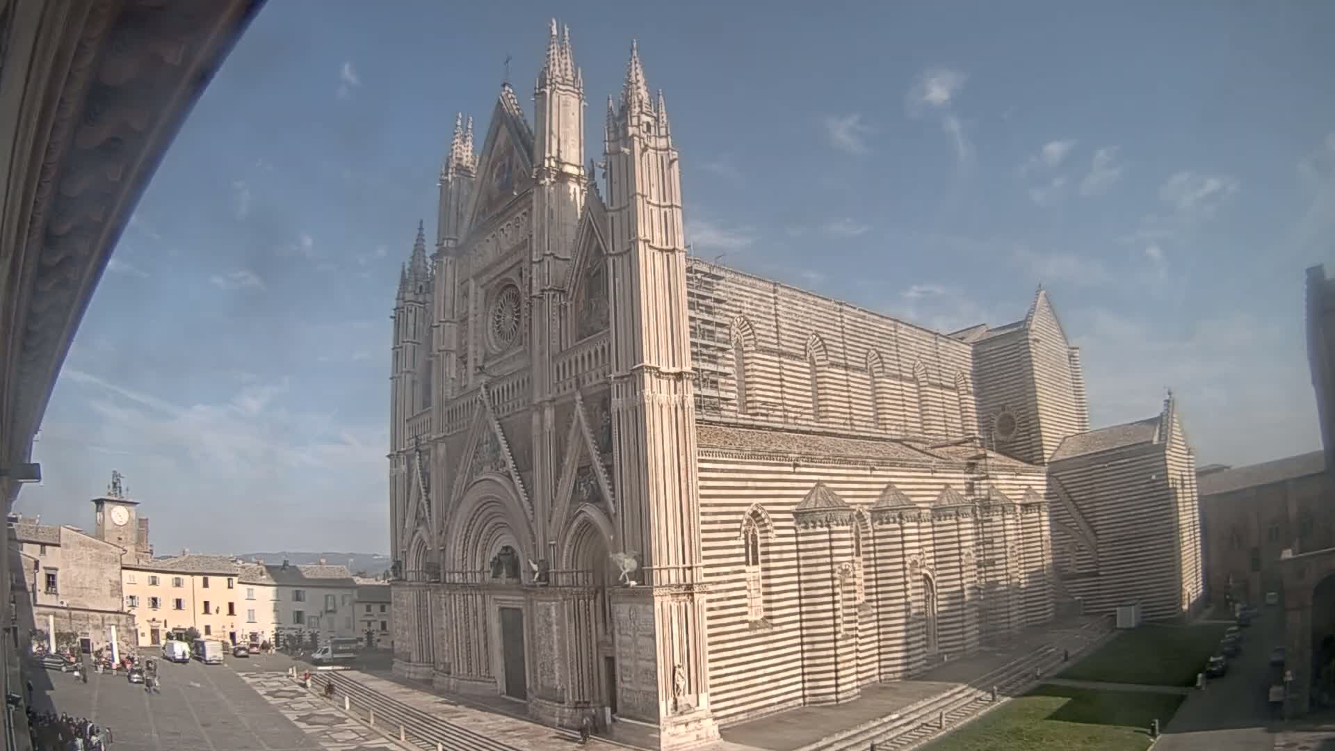 A large, striped stone cathedral stands in a town square on a partly sunny day.