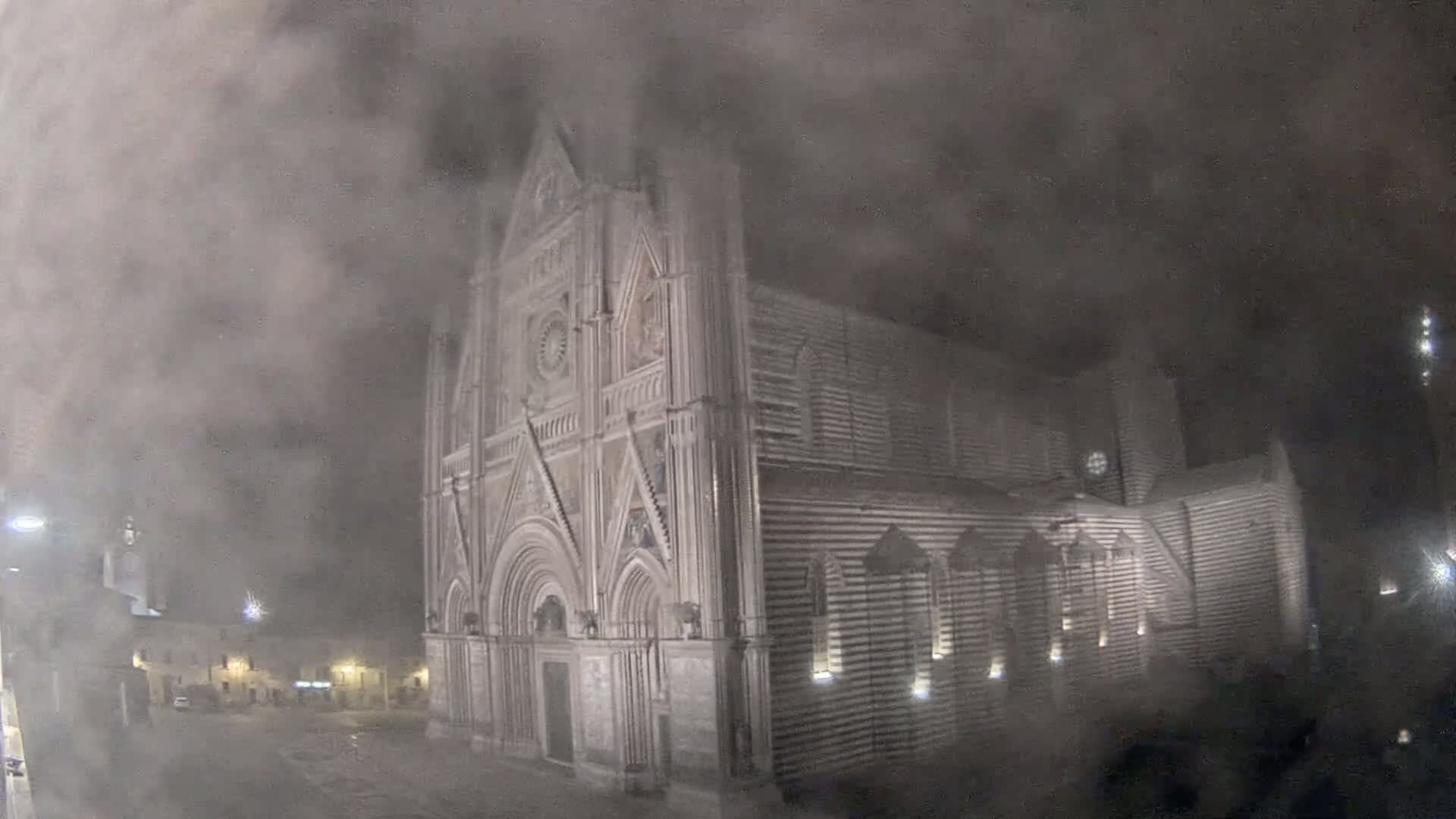 A large stone cathedral is partially obscured by heavy fog or mist at night.