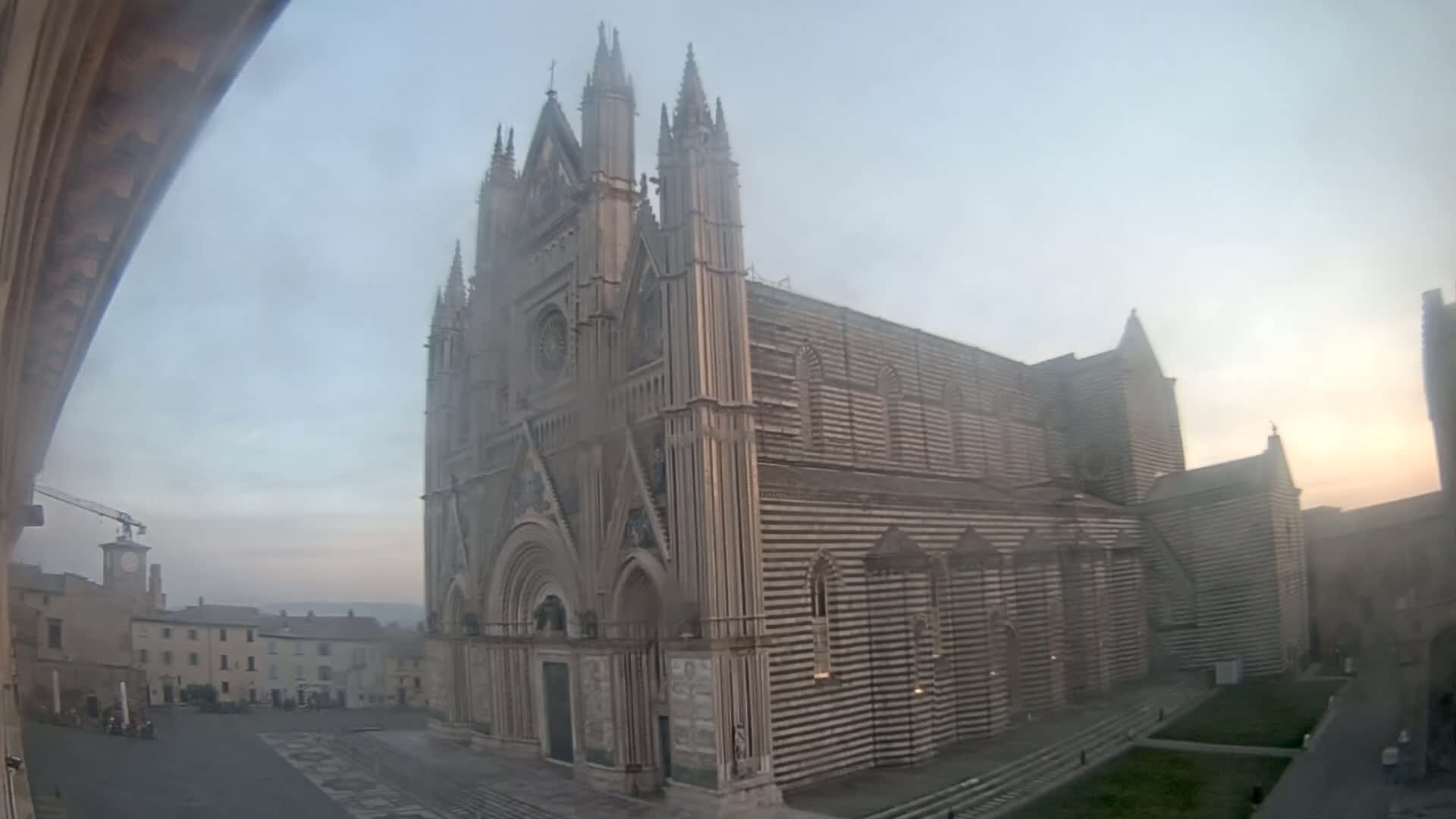 A large, striped cathedral stands in a town square on a hazy morning.