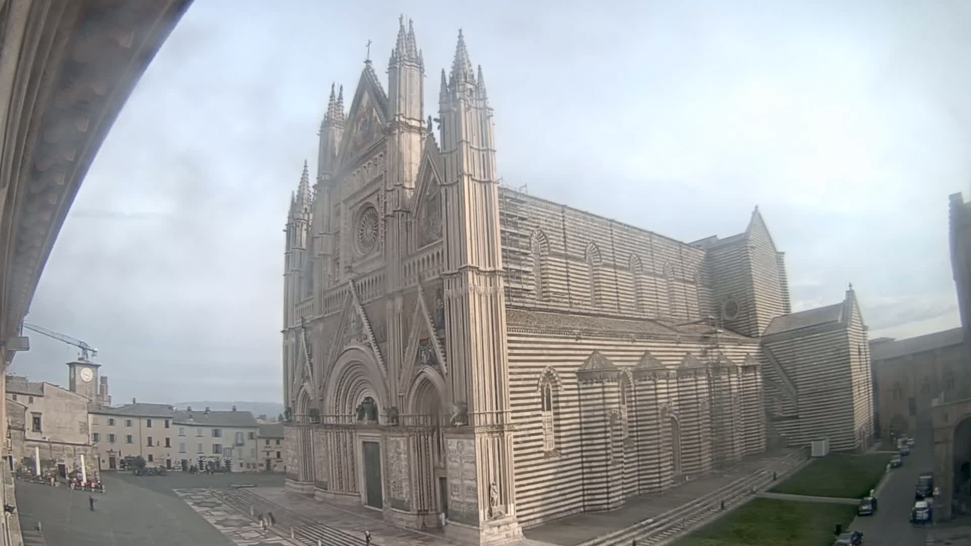 A large, striped cathedral with Gothic architecture stands in a town square on an overcast day.