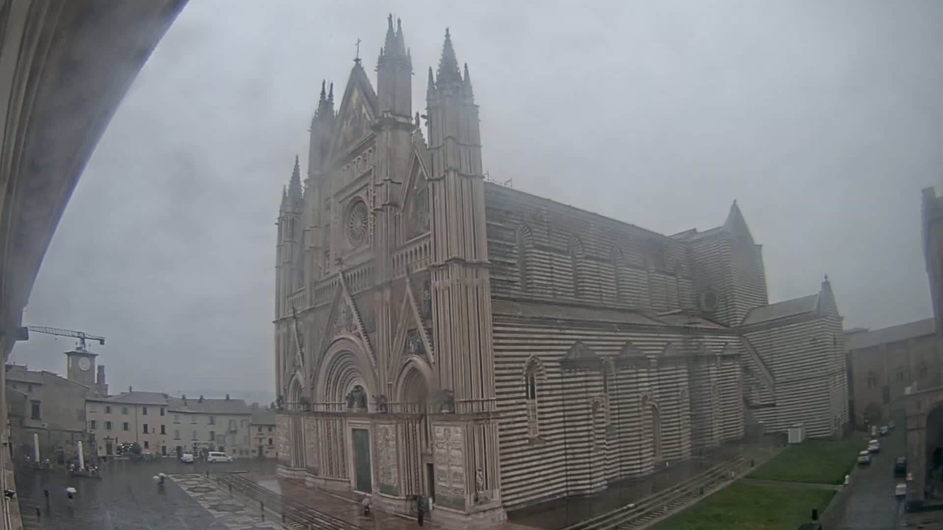 A large, striped cathedral stands in a town square on a rainy day.