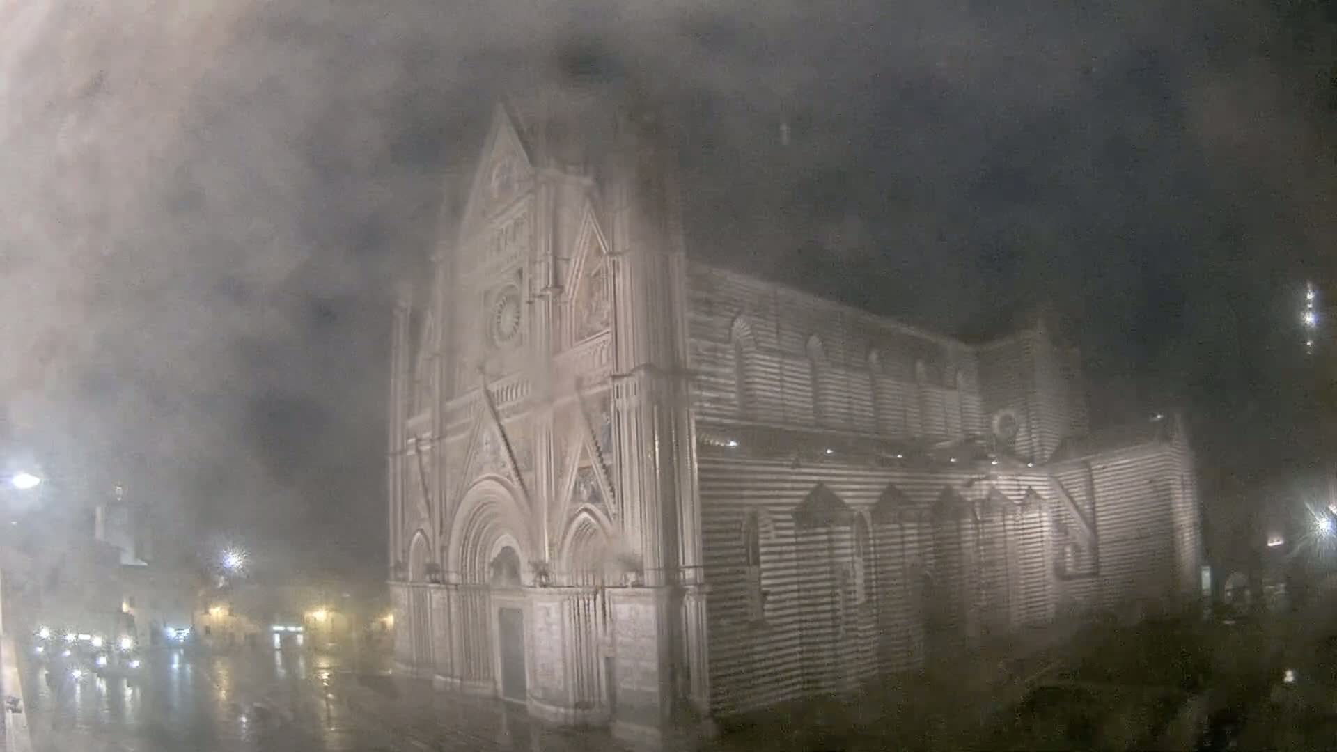 A large, striped stone cathedral is seen at night in heavy fog and rain.