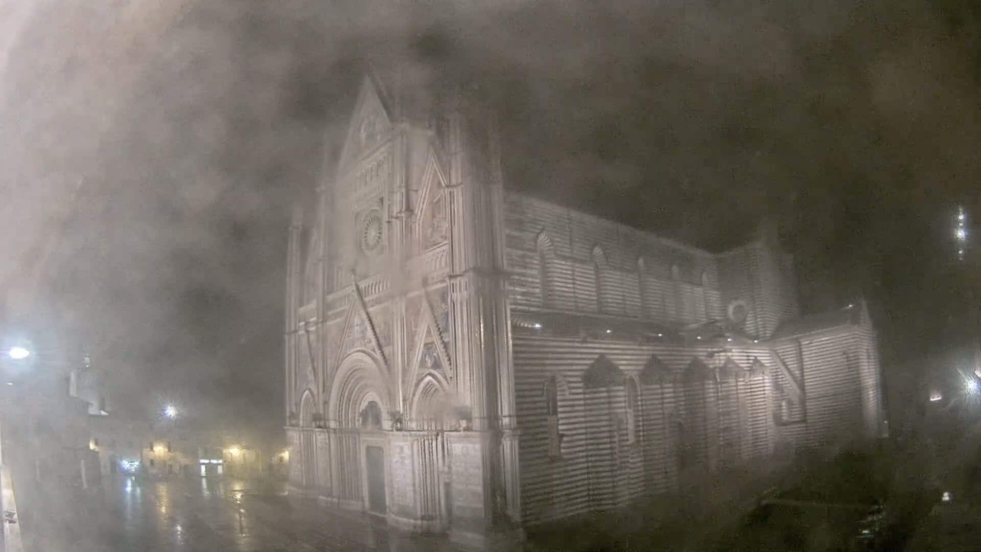 A large, striped stone cathedral is seen at night in heavy fog and rain.