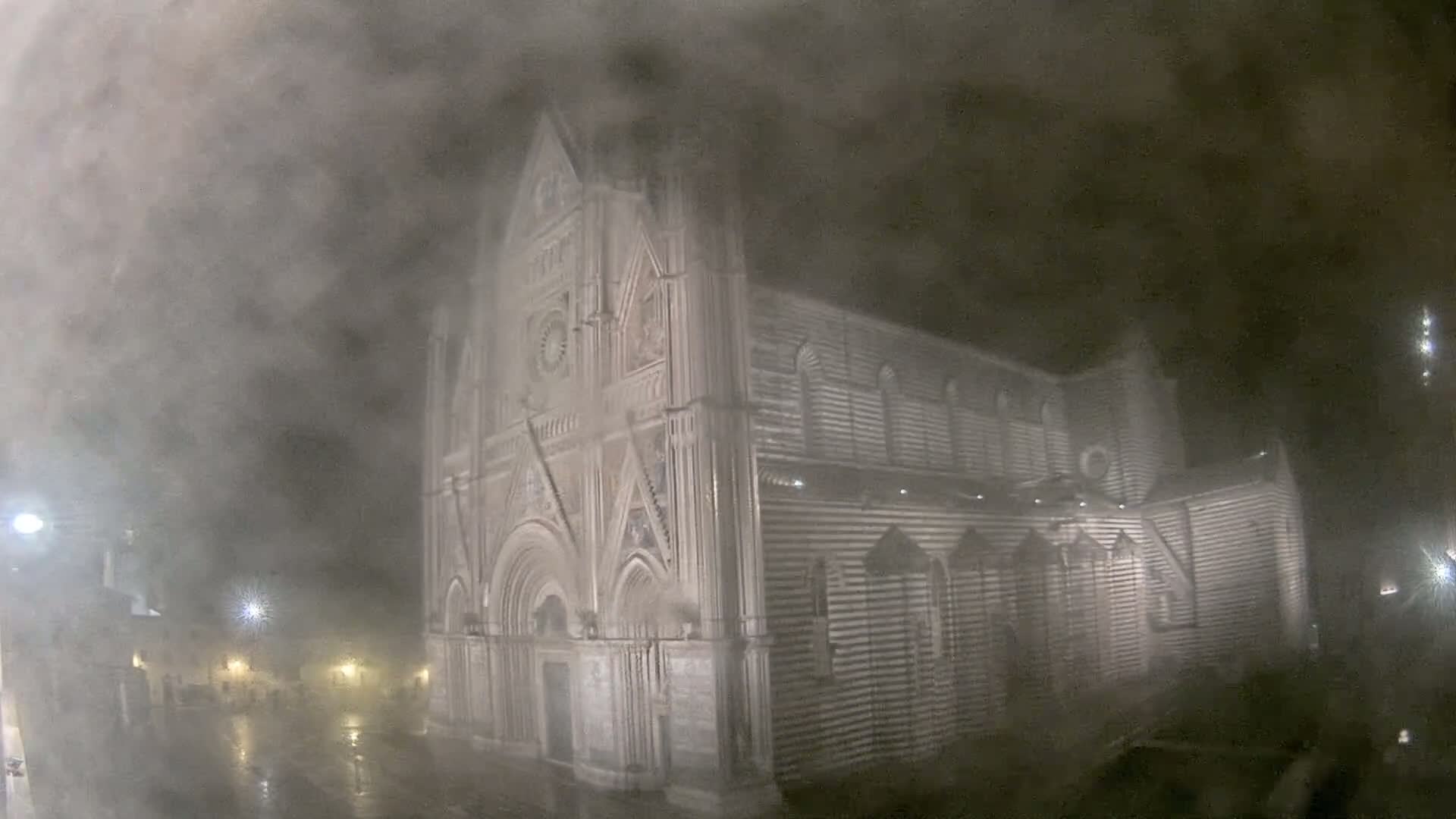 A large, striped stone church is seen at night in heavy fog and rain.