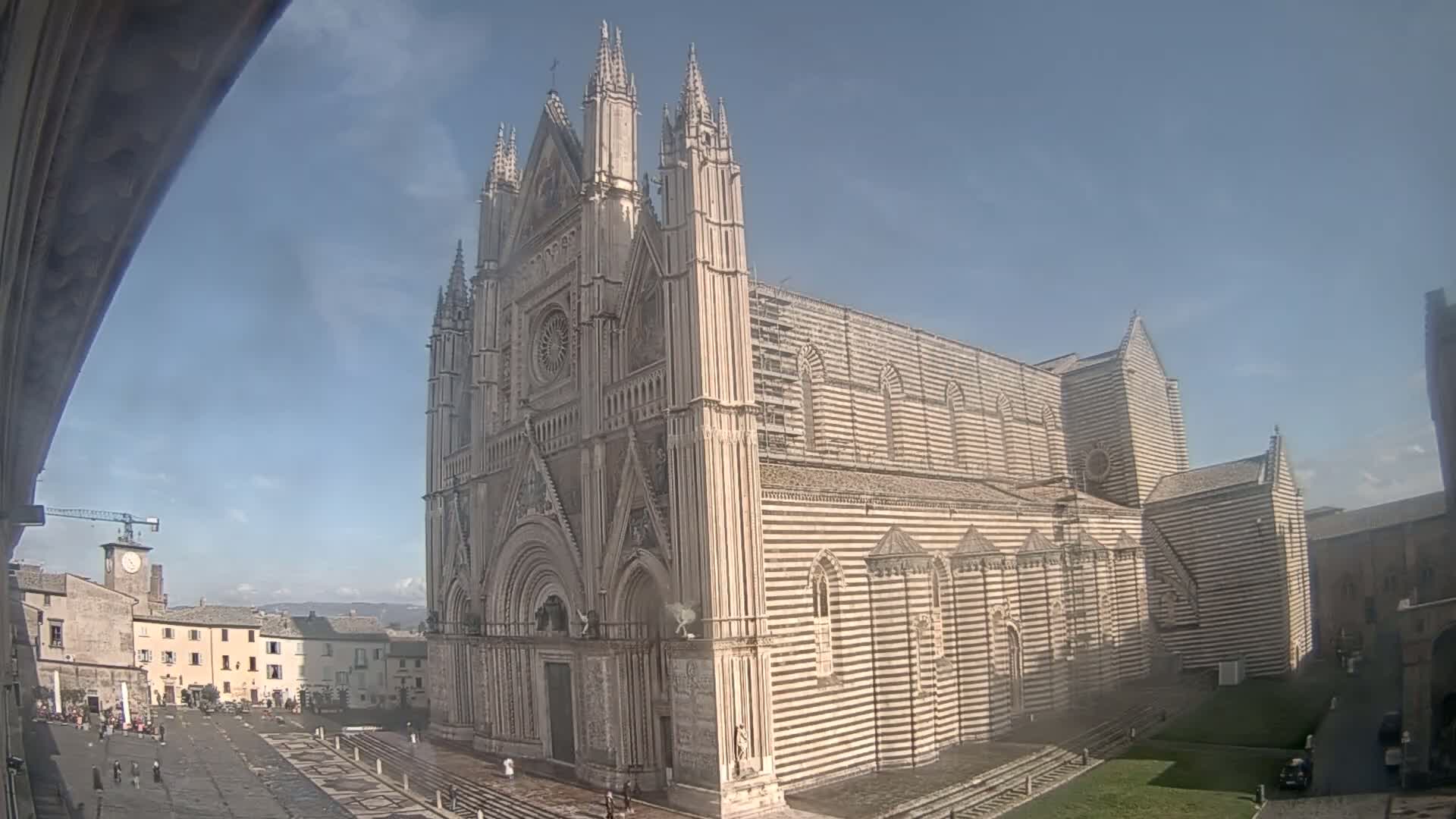 A large, striped cathedral stands in a town square under a mostly clear sky.
