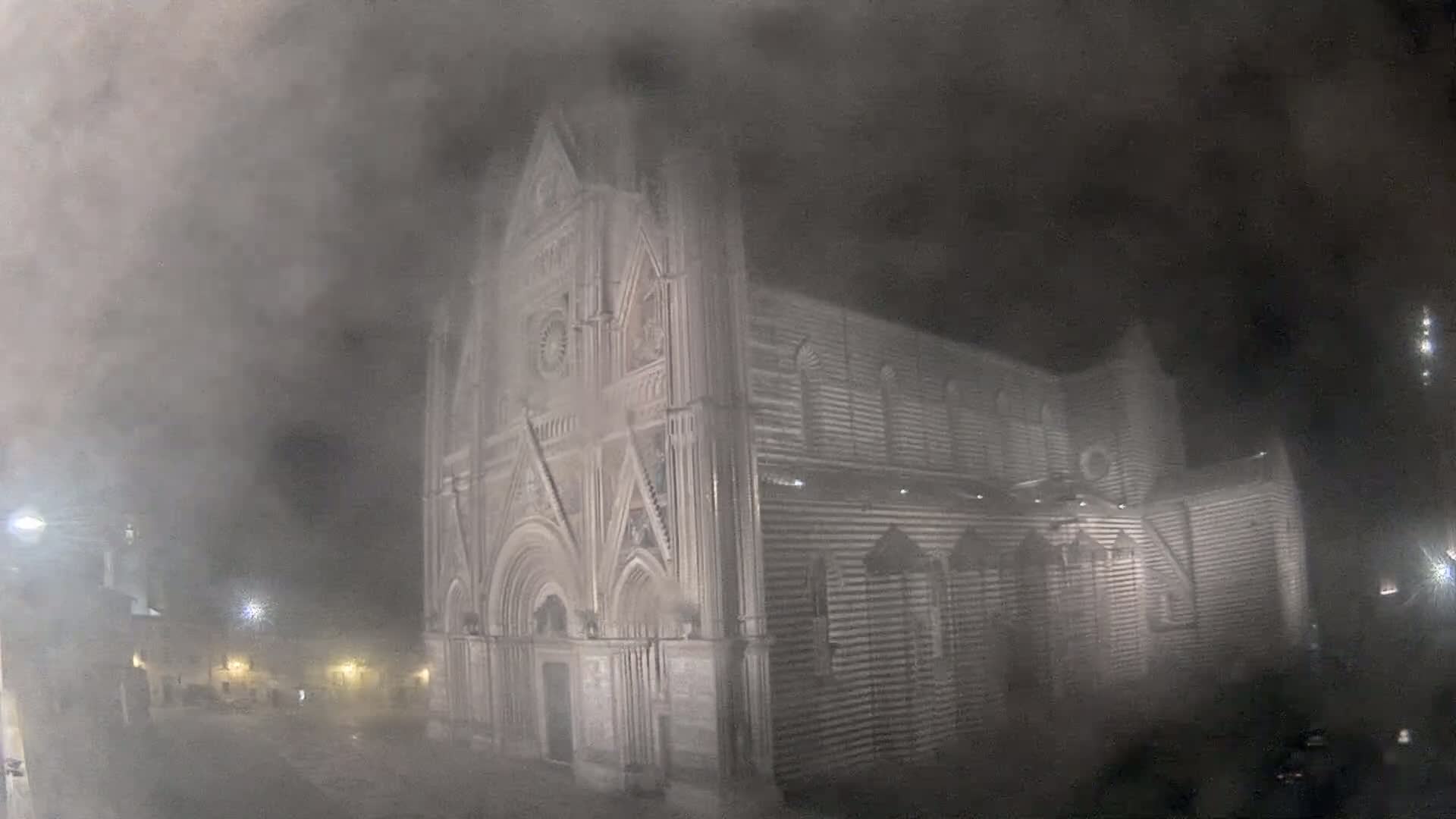 A large, striped stone cathedral is partially obscured by a thick fog at night.