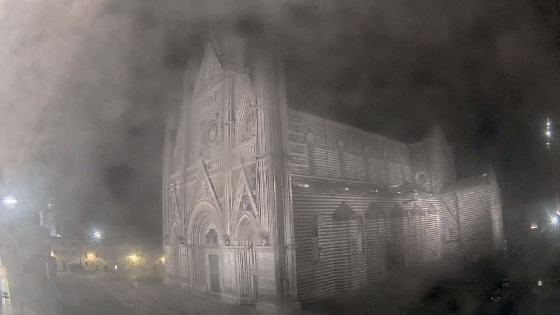 A large stone cathedral is partially obscured by heavy fog at night.