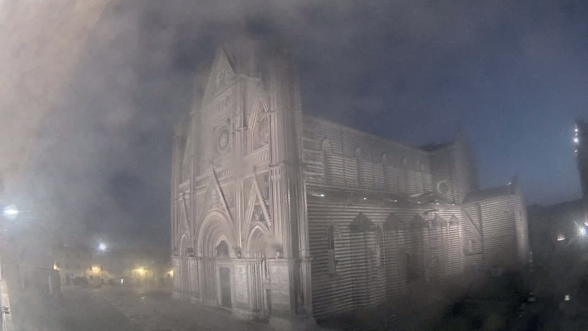 A large, striped stone cathedral stands under a foggy, dark night sky.