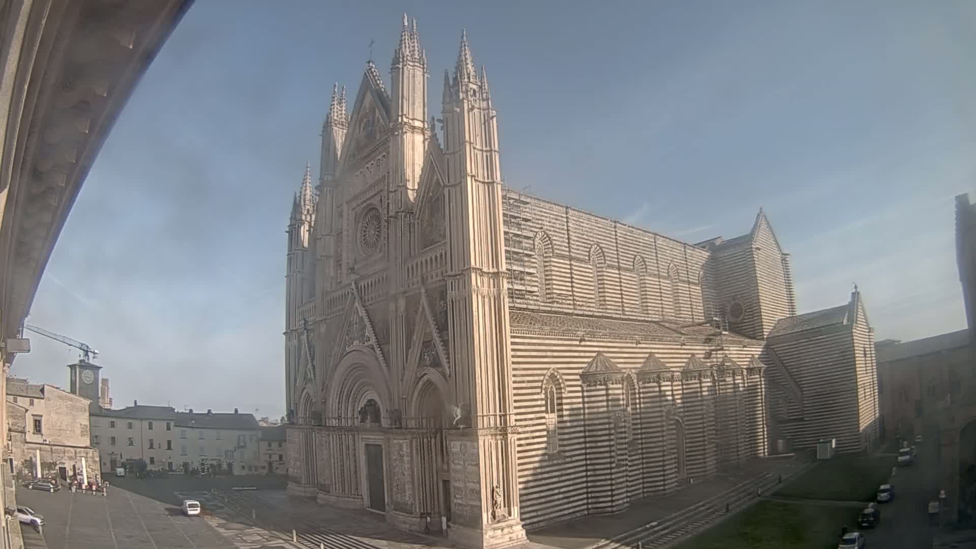 A large, striped cathedral stands in a town square on a mostly sunny day.