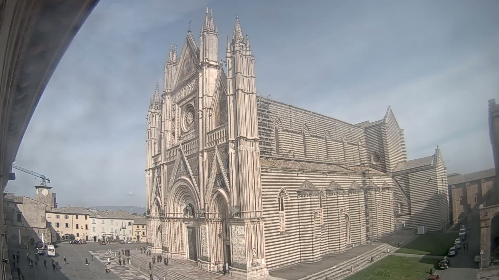A large, striped stone cathedral stands in a town square on a partly cloudy day.