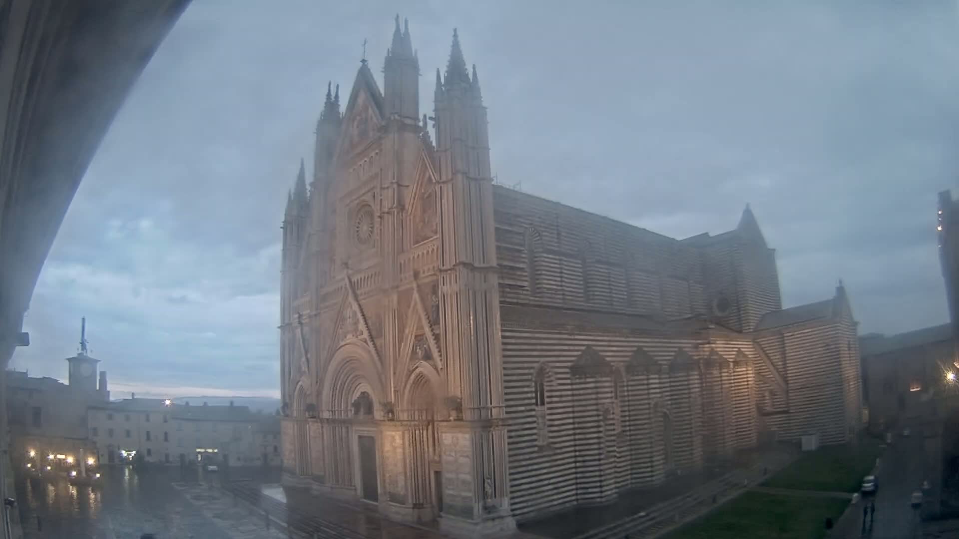 A large, striped cathedral stands in a town square during a rainy, overcast day.
