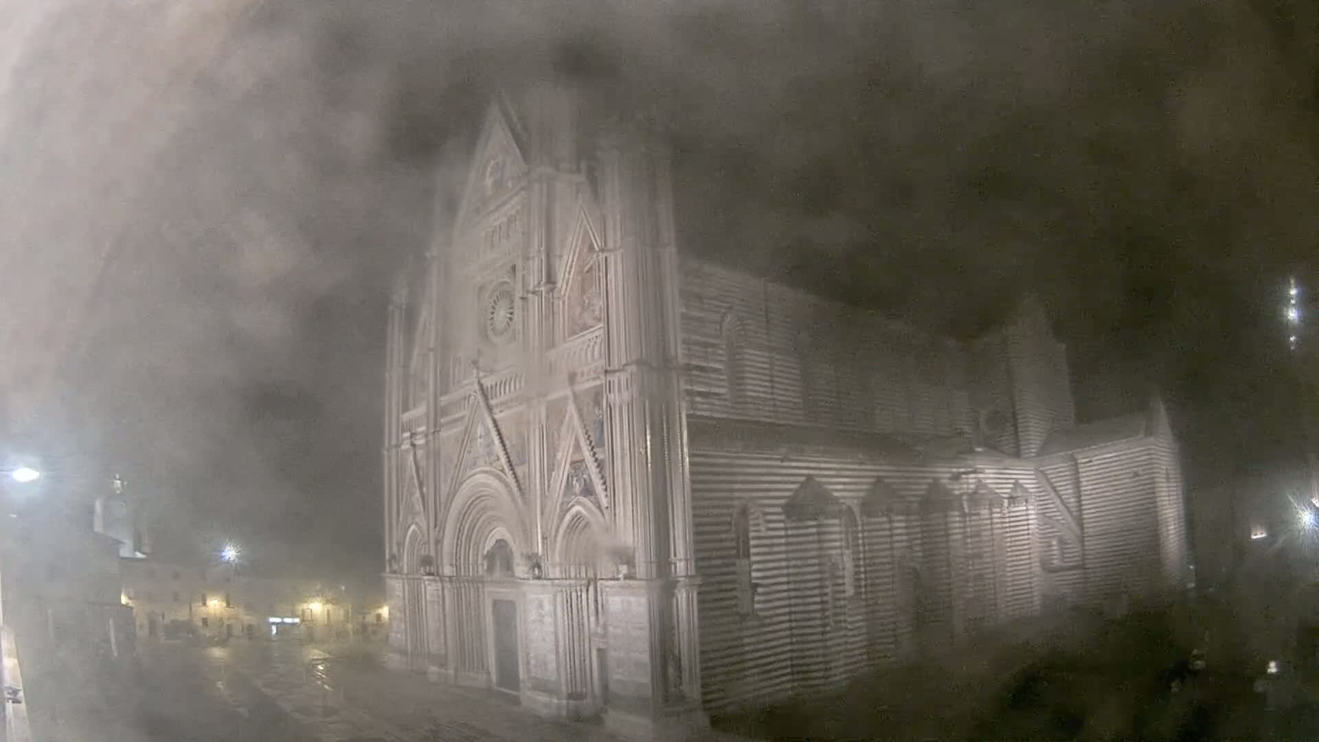 A large, striped stone cathedral stands at night in a heavy fog or mist.