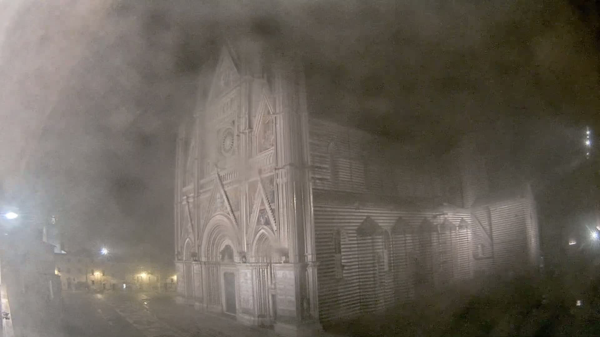 A large stone cathedral is shrouded in thick fog at night.