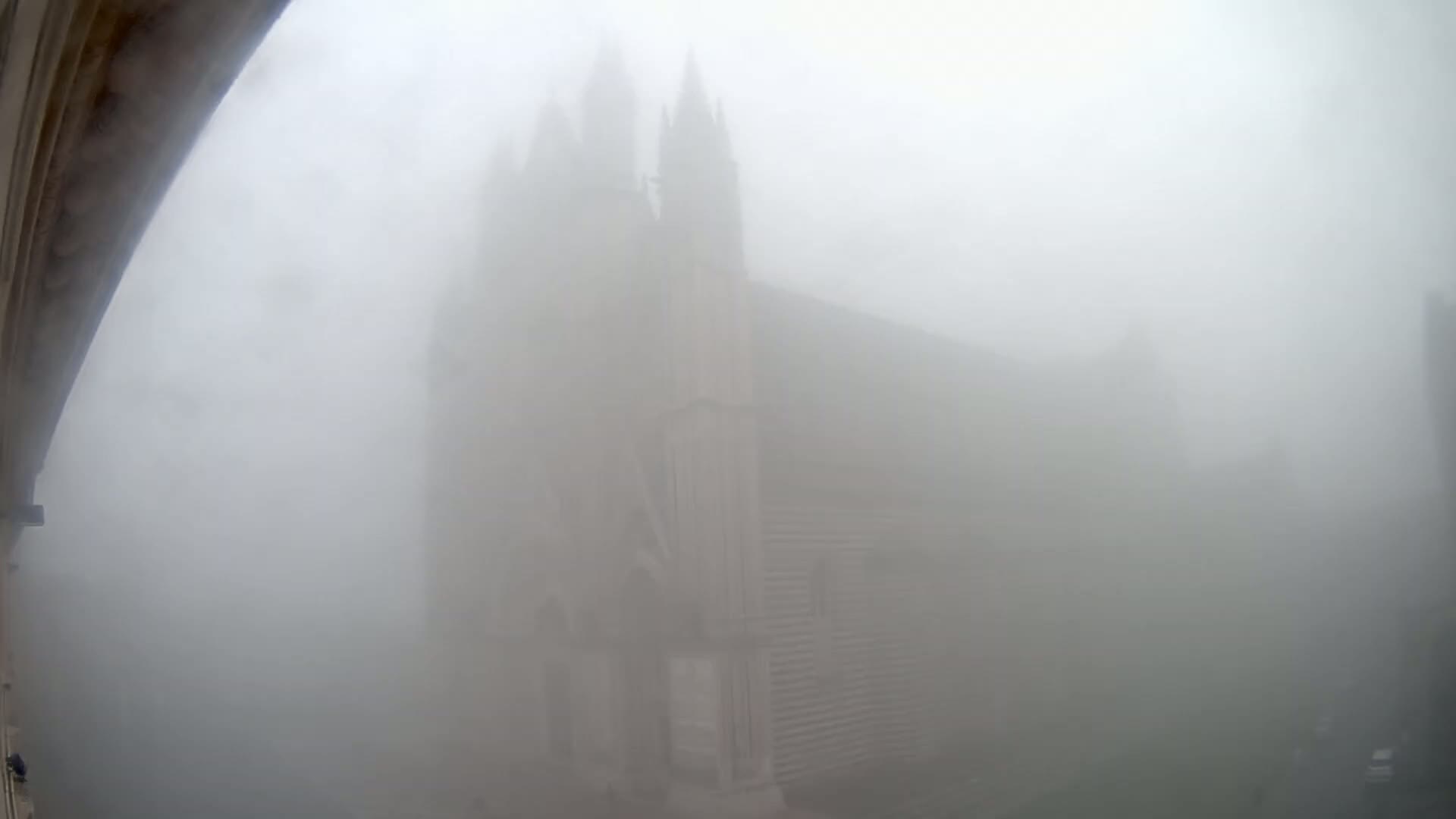 A large stone church is barely visible through a thick fog.