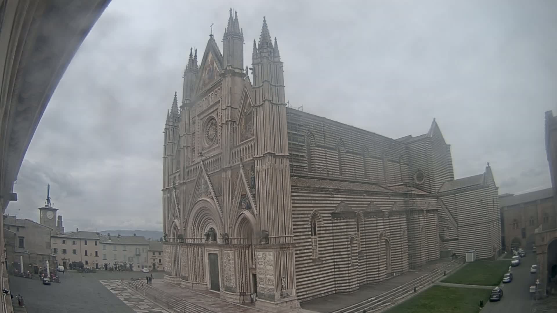 A large, striped cathedral stands in a town square on an overcast day.