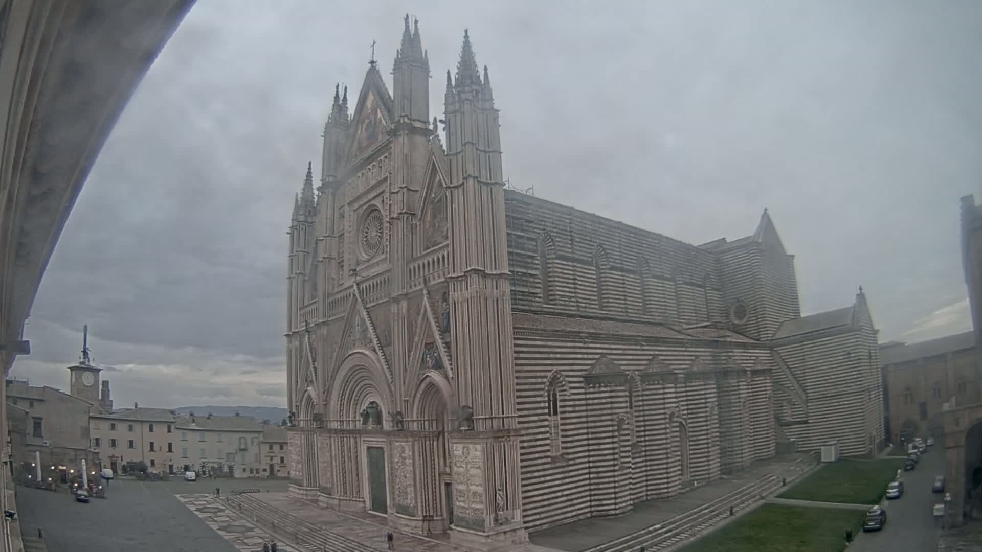A large, striped stone cathedral stands in a town square on an overcast day.