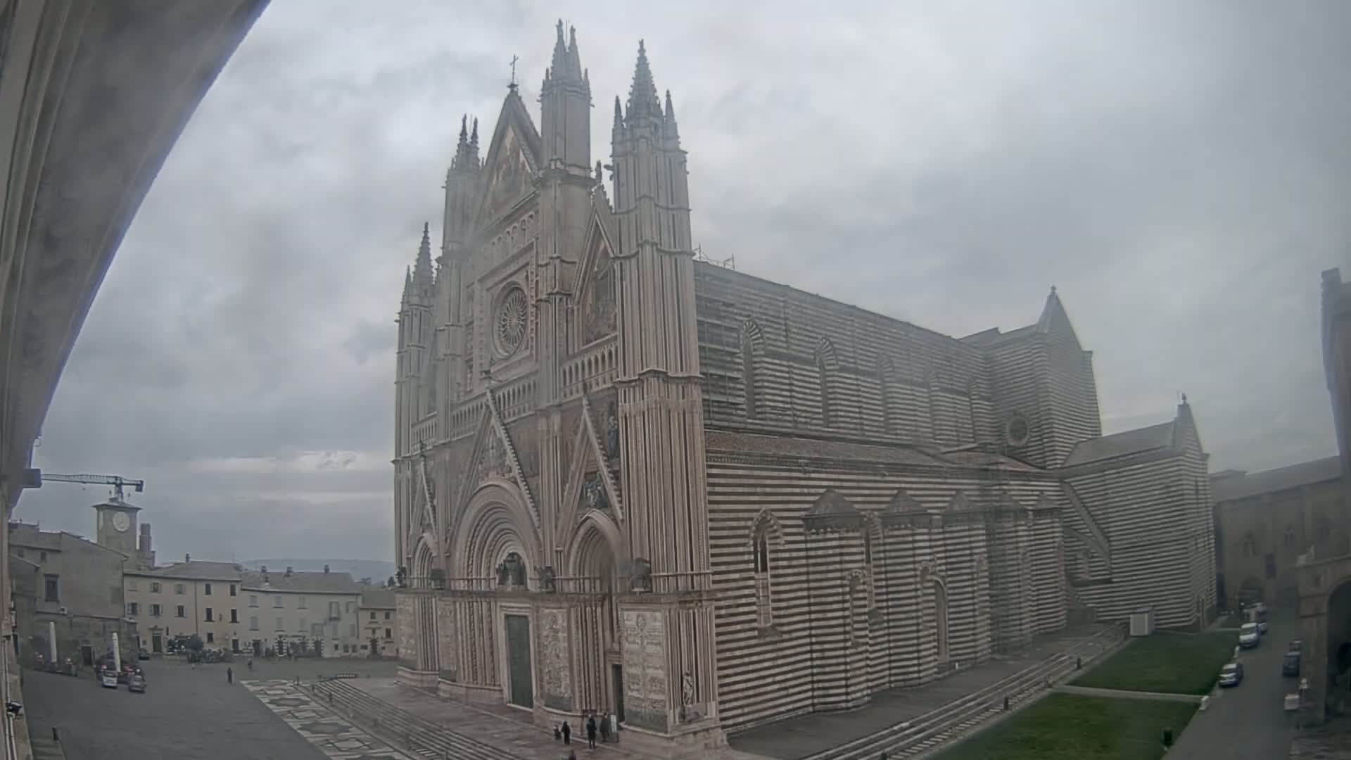 A large, striped cathedral stands in a town square on an overcast day.