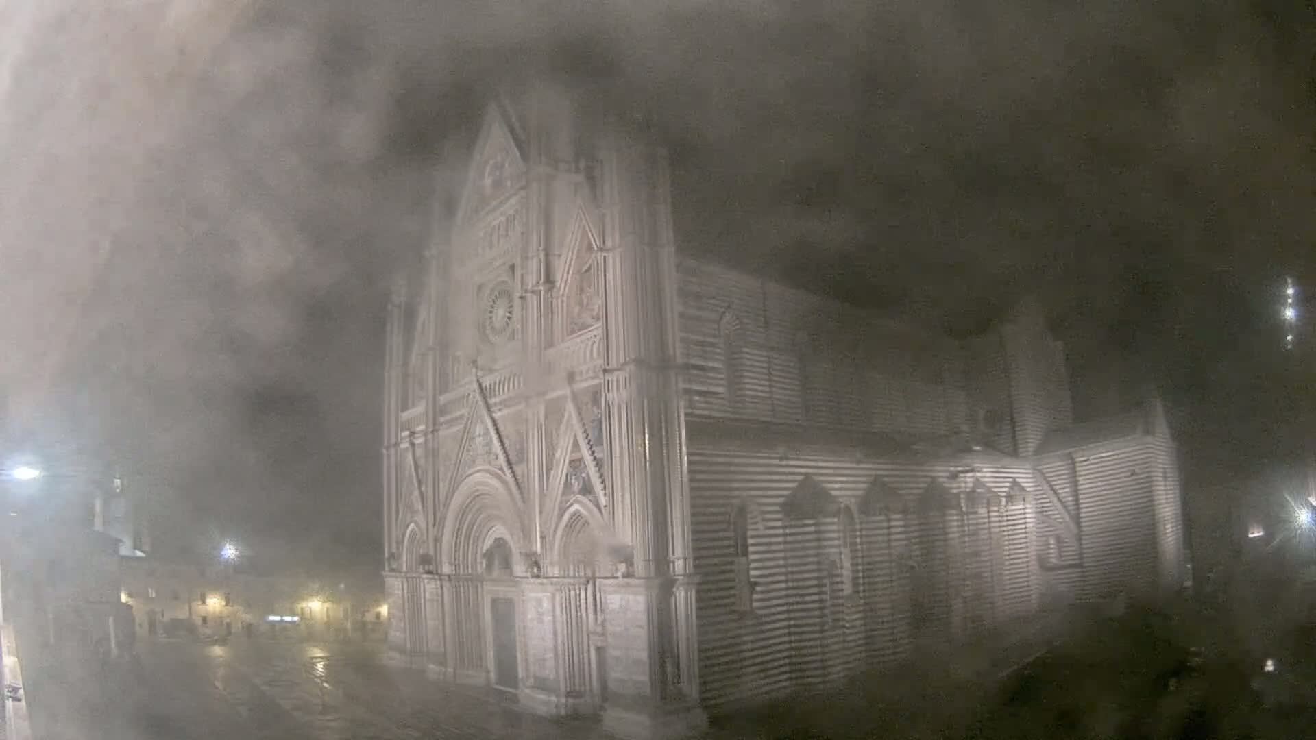 A large, striped stone cathedral is partially obscured by heavy fog and rain at night.