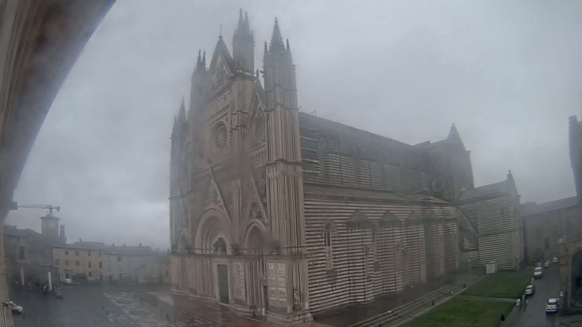 A large, striped cathedral stands in a town square on a foggy day.