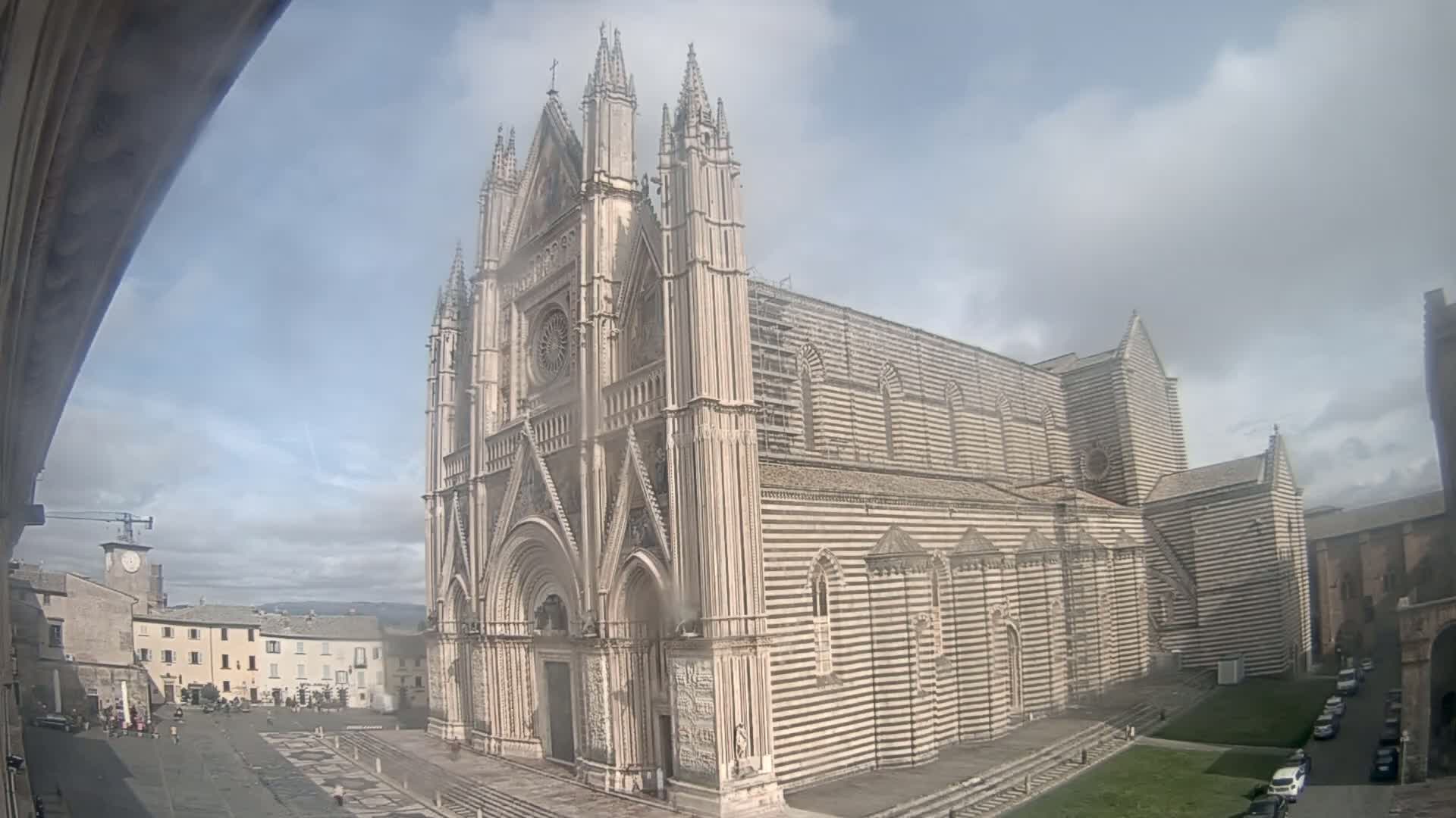 A large, striped cathedral stands in a town square on a partly cloudy day.