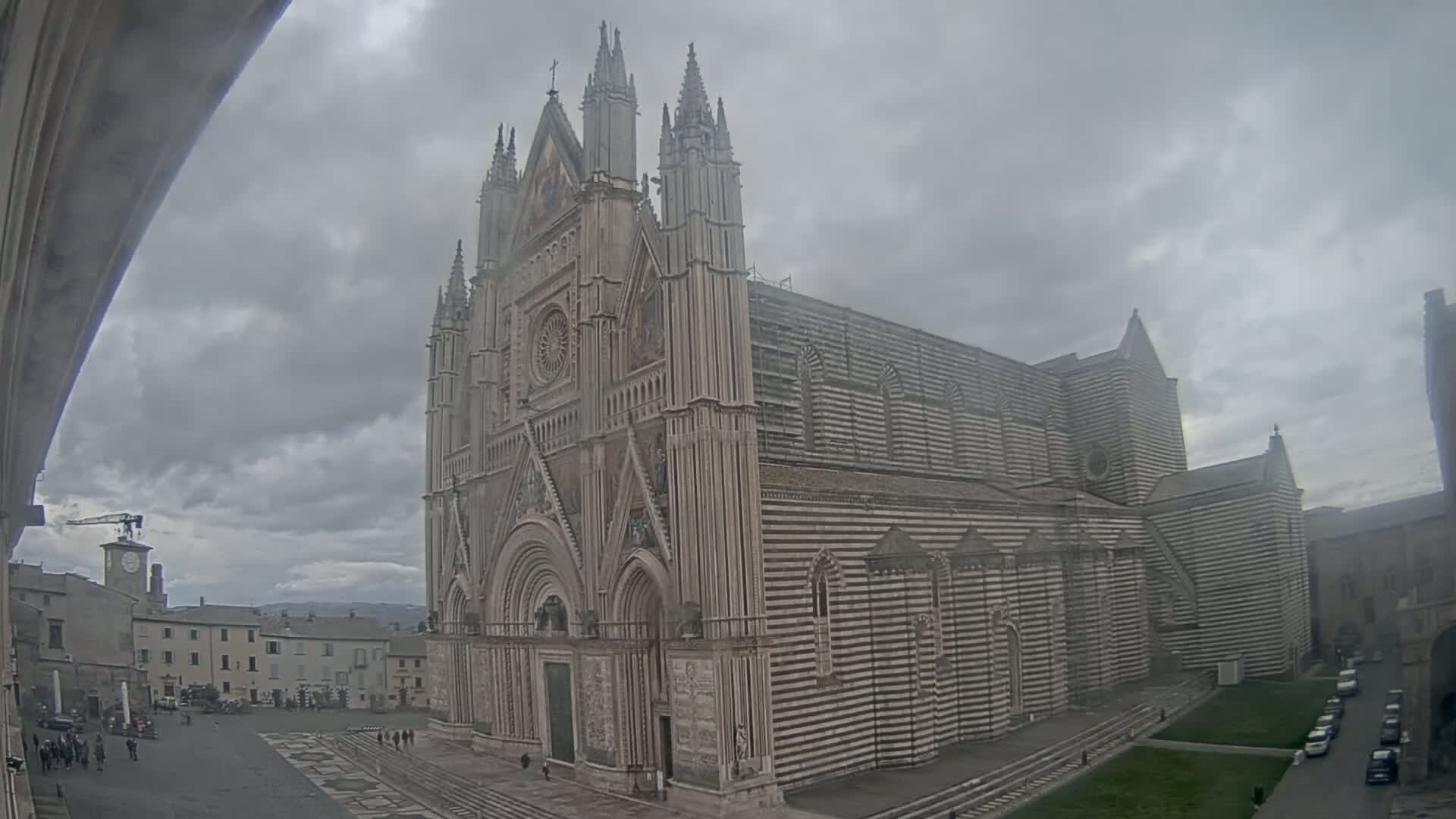 A large, striped stone cathedral stands in a town square on an overcast day.
