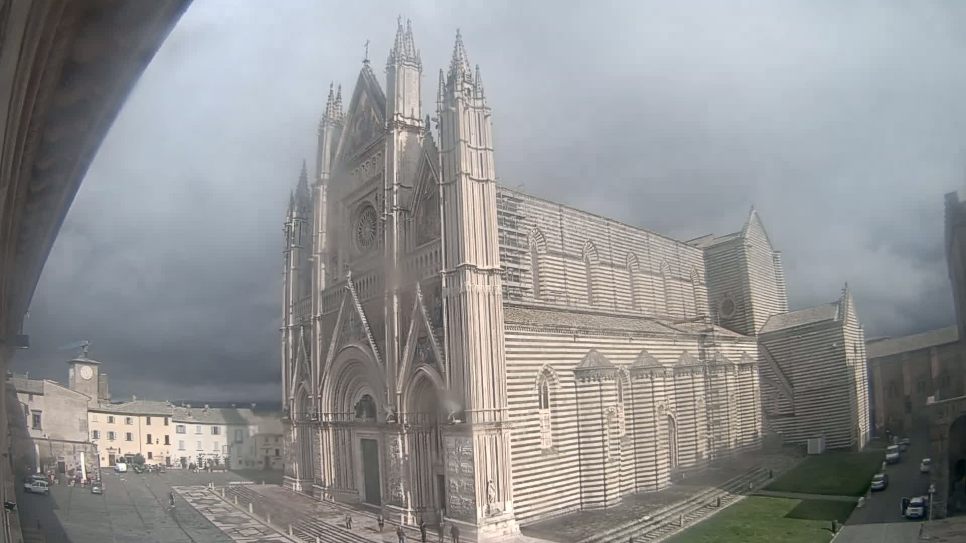 A large, striped cathedral stands in a town square under a cloudy sky.