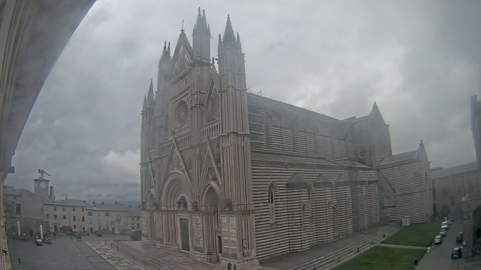 A large, striped cathedral stands in a town square on an overcast day.