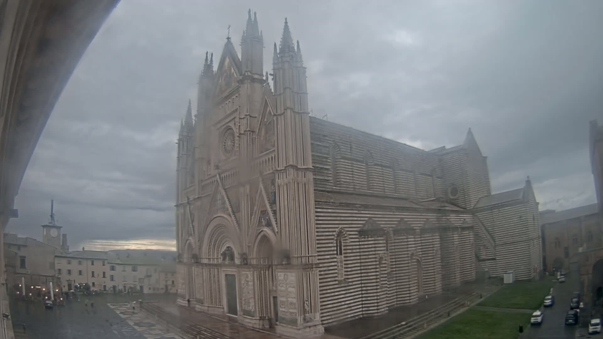 A large, striped cathedral stands in a town square on a rainy, overcast day.
