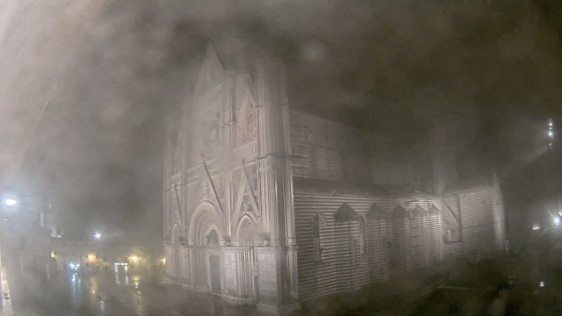 A large, ornate stone church is partially obscured by heavy fog and rain at night.