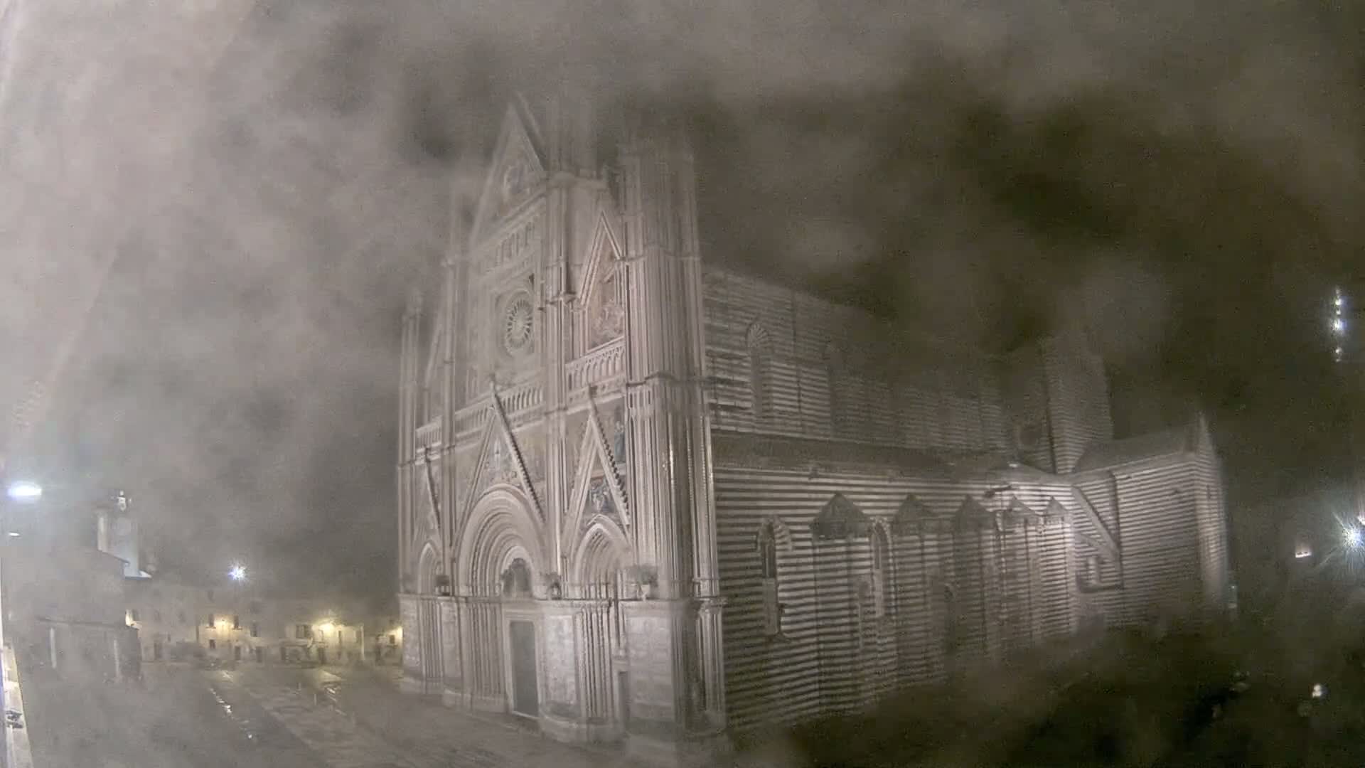 A large, striped cathedral is partially obscured by heavy fog or mist at night.