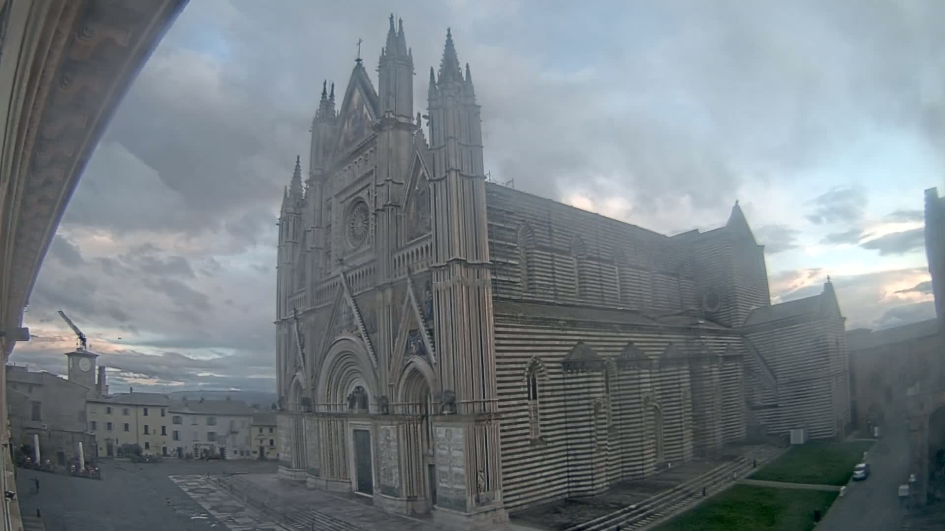 A large, striped, Gothic-style cathedral stands in a town square under a cloudy sky.