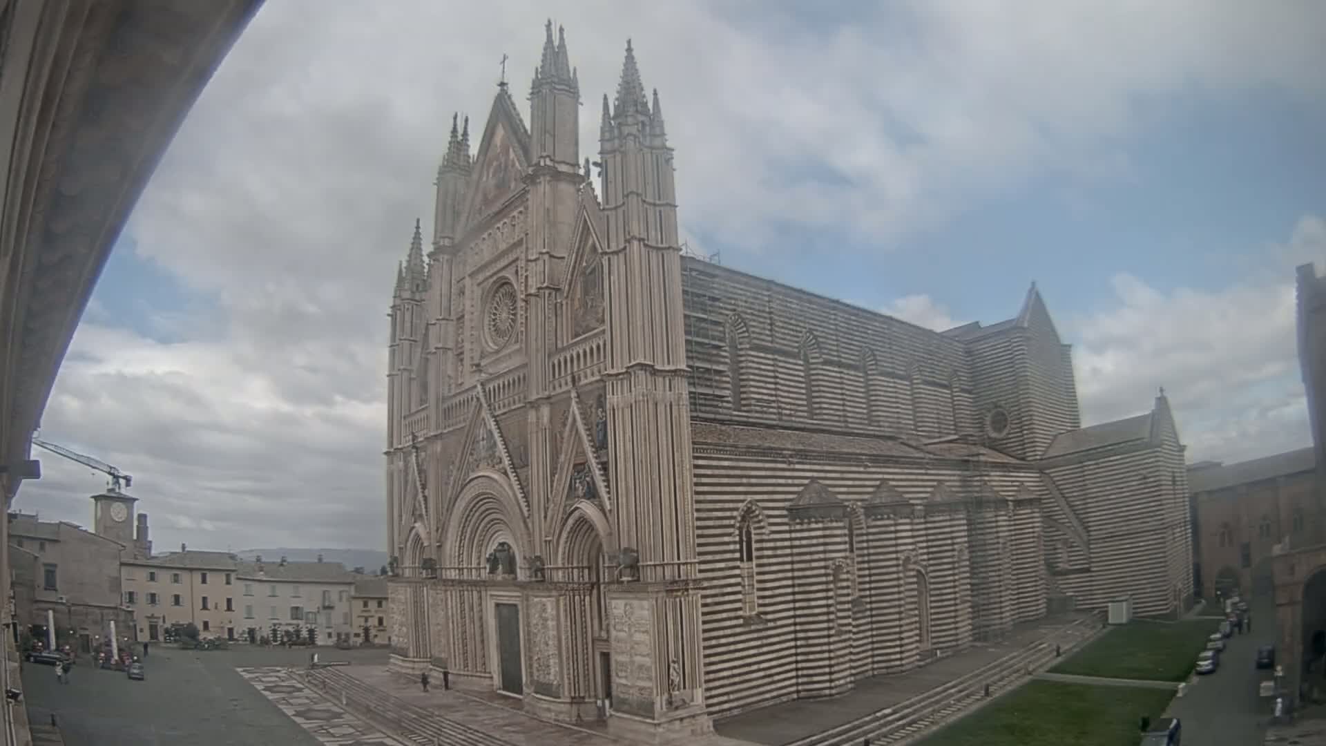 A large, striped cathedral stands in a town square under a cloudy sky.