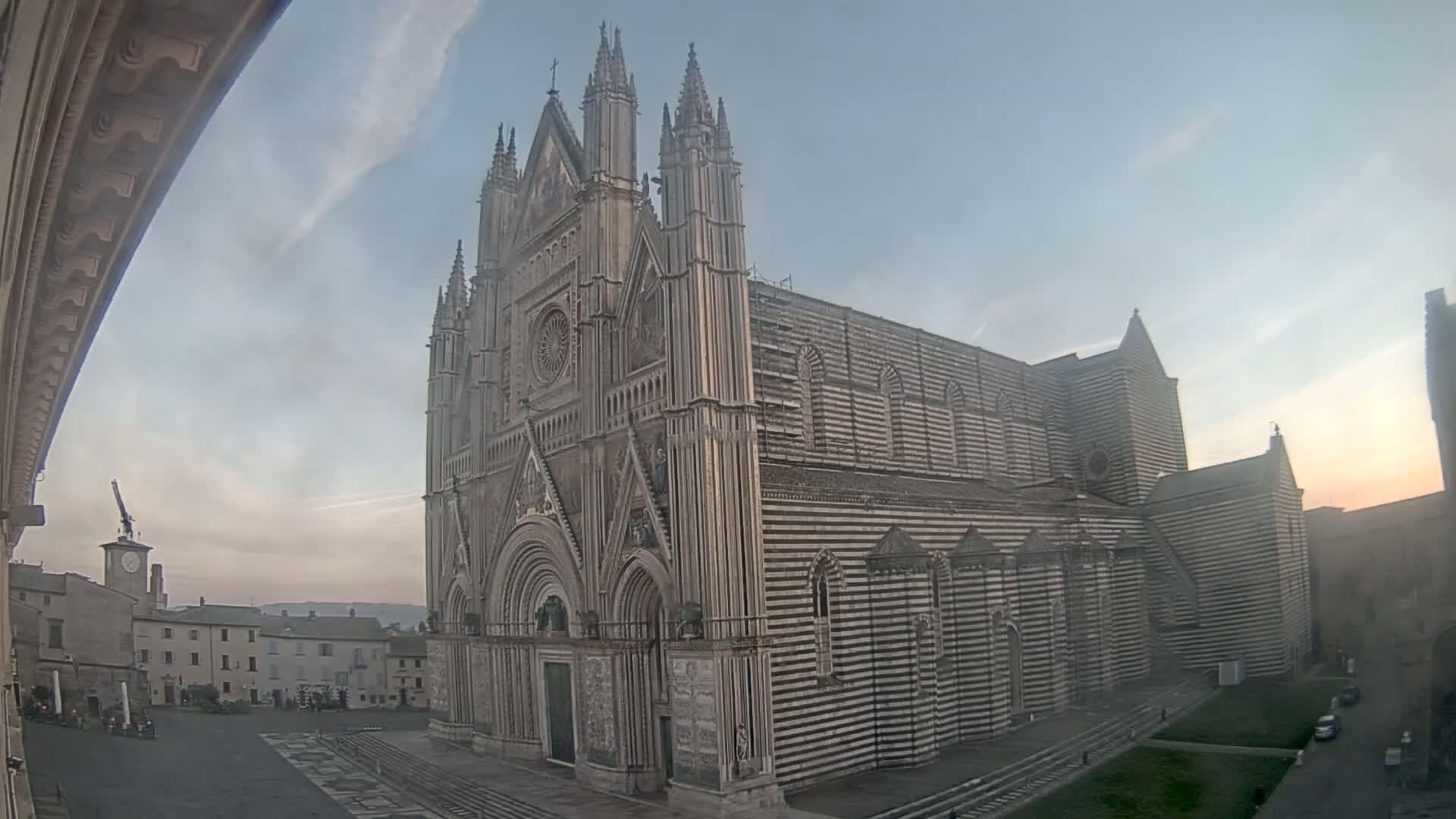 A large, striped cathedral stands in a town square under a mostly clear, twilight sky.