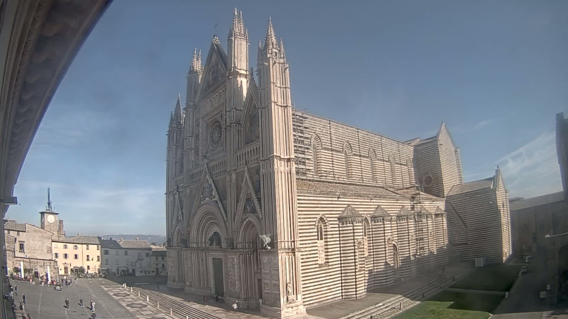 A large, striped cathedral stands in a town square on a sunny day.