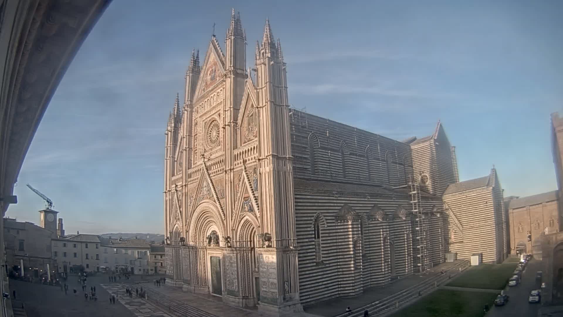 A large striped cathedral stands in a city square on a clear, sunny day.