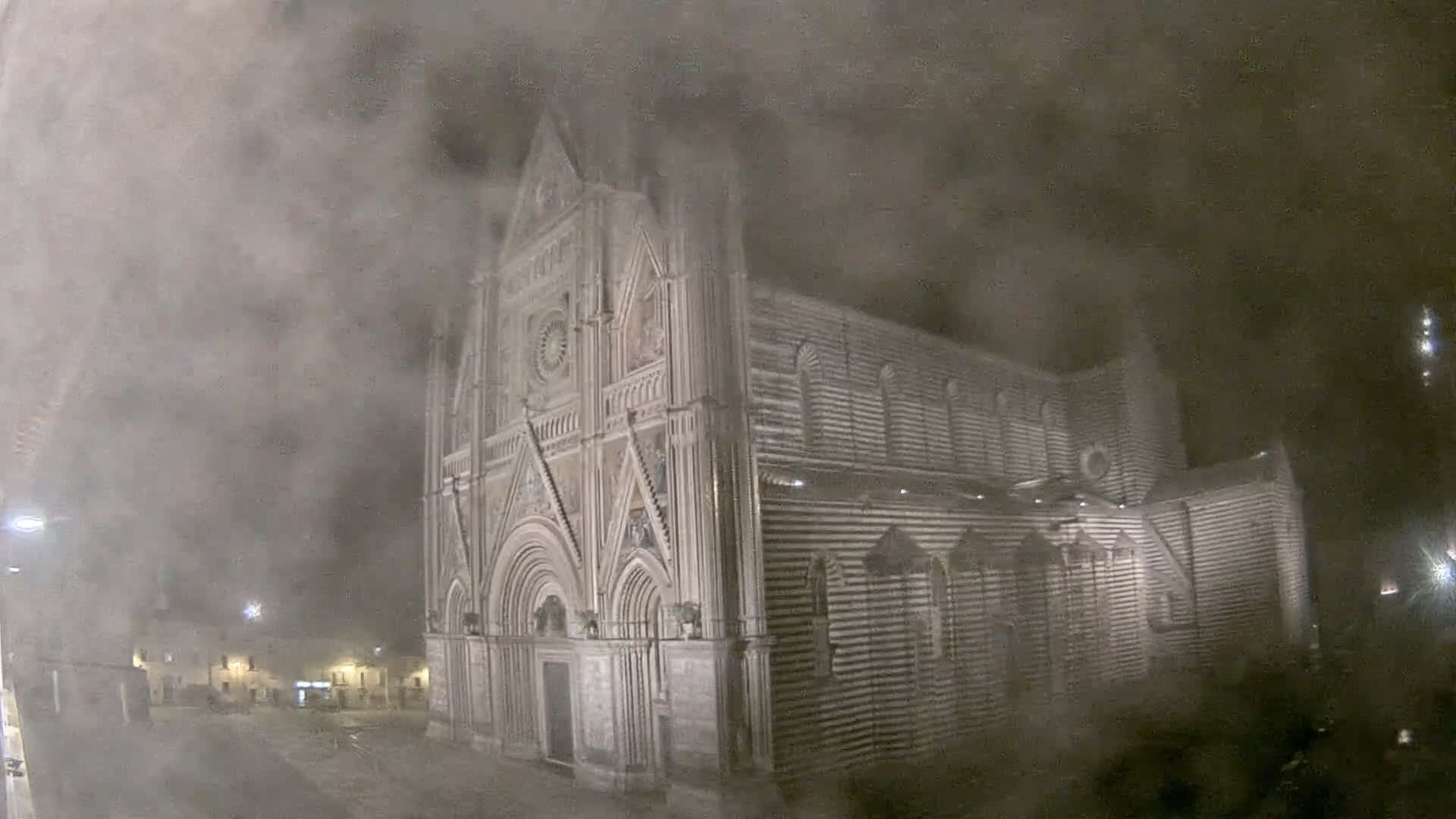 A large, ornately decorated stone cathedral is seen at night in a heavy fog or snow.