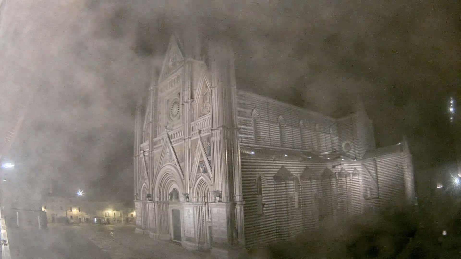 A large, ornate stone cathedral is partially obscured by a thick fog at night.