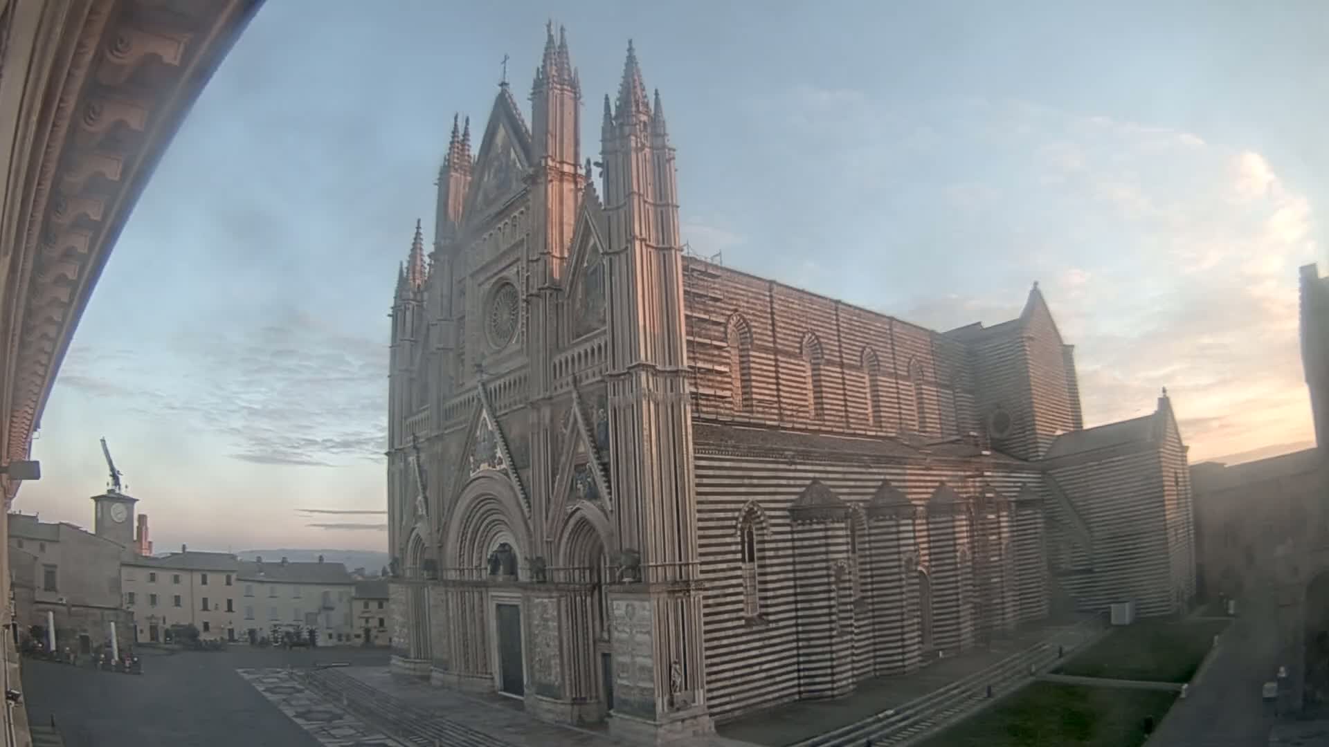 A large, striped stone cathedral stands in a town square under a mostly clear, twilight sky.