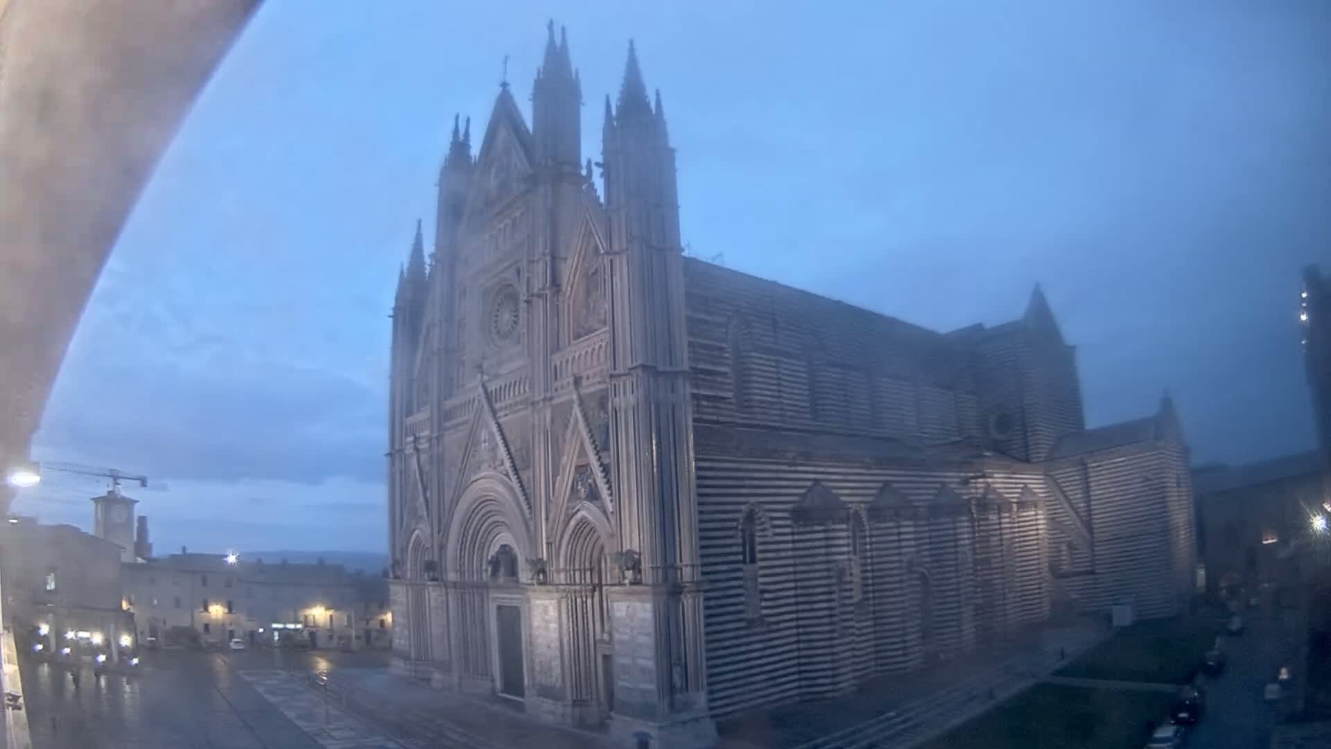 A large, striped cathedral stands in a town square on a misty, overcast evening.