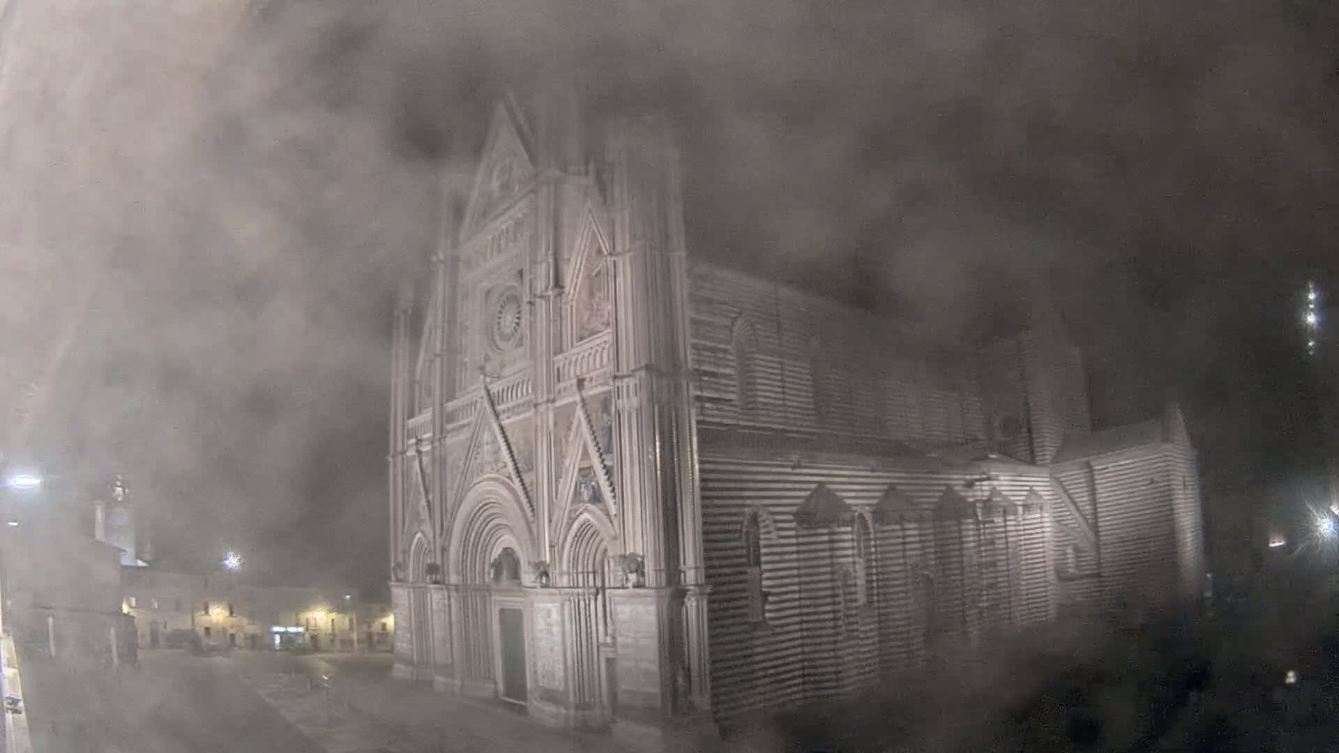 A large, striped stone cathedral is partially obscured by thick fog at night.