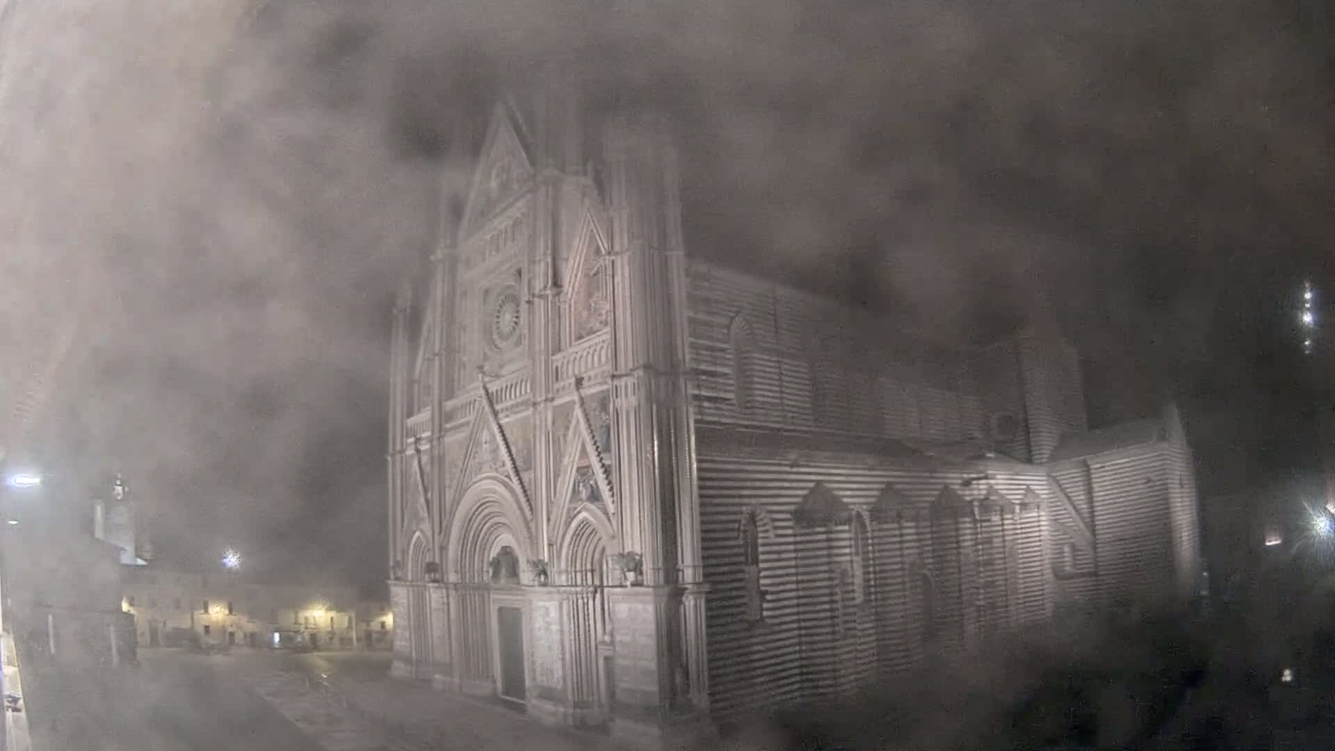 A large, ornate stone cathedral is partially obscured by heavy fog at night.
