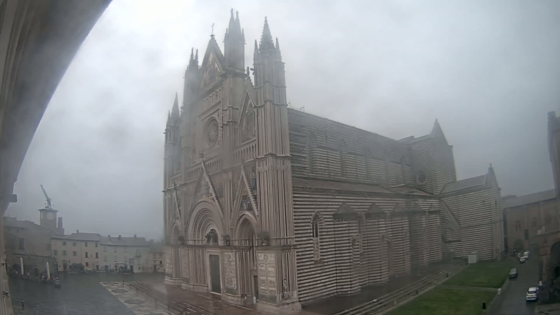 A large, striped cathedral stands in a town square on a foggy, rainy day.