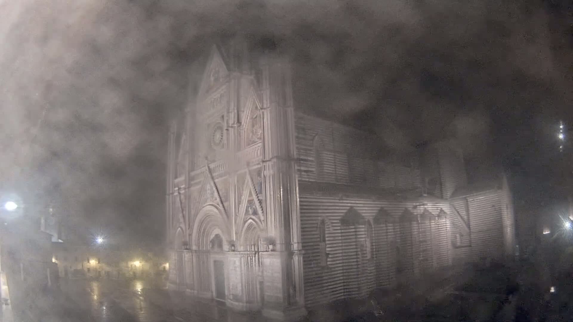 A large, striped stone cathedral is shrouded in thick fog and rain at night.