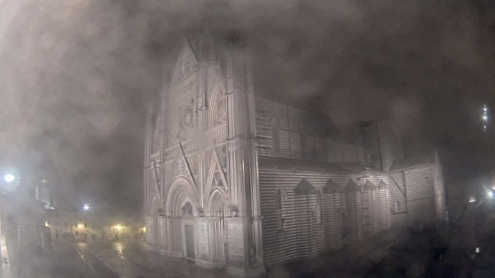 A large, striped stone cathedral stands shrouded in heavy fog or mist at night.